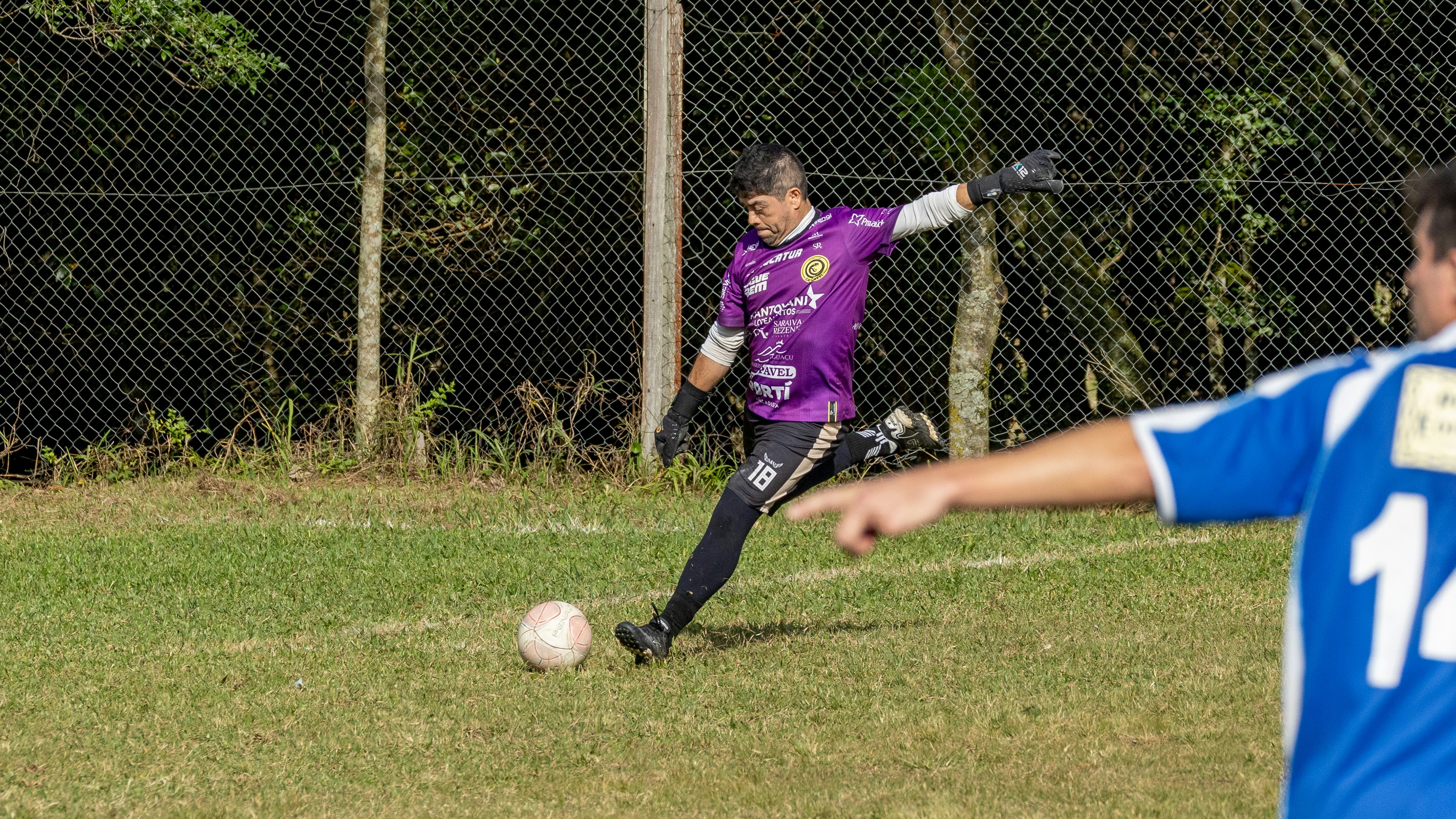 Kiper berseragam ungu menendang bola sepak di lapangan berumput.