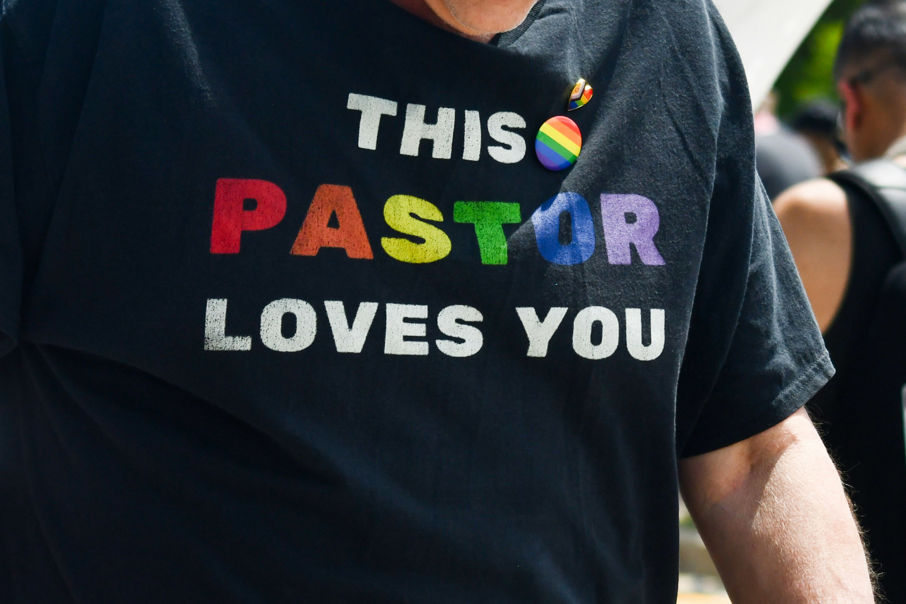 Black t-shirt displaying 'this pastor loves you' in rainbow text.