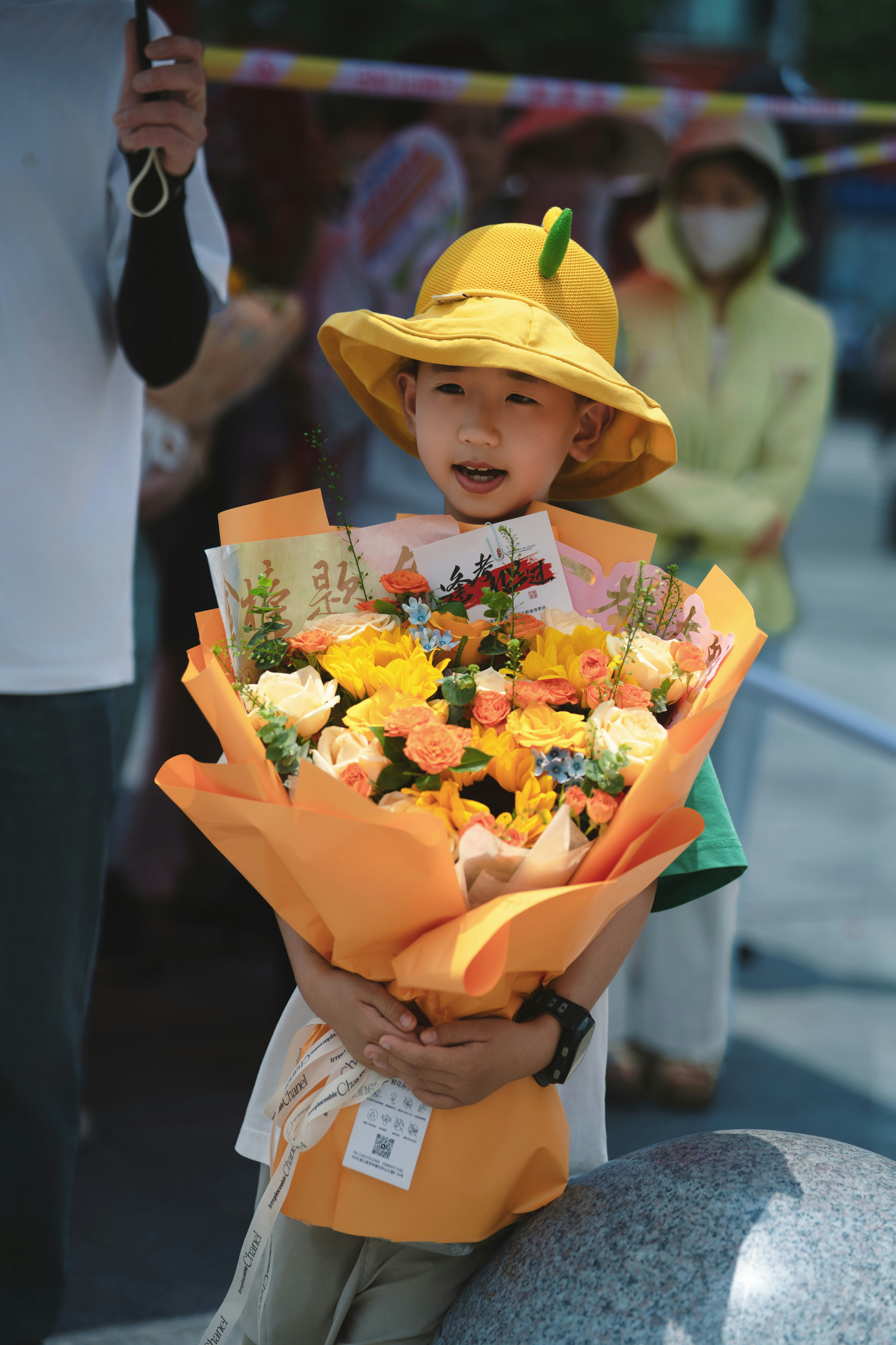 Glückliches Kind mit gelbem Hut hält einen bunten Blumenstrauß draußen.