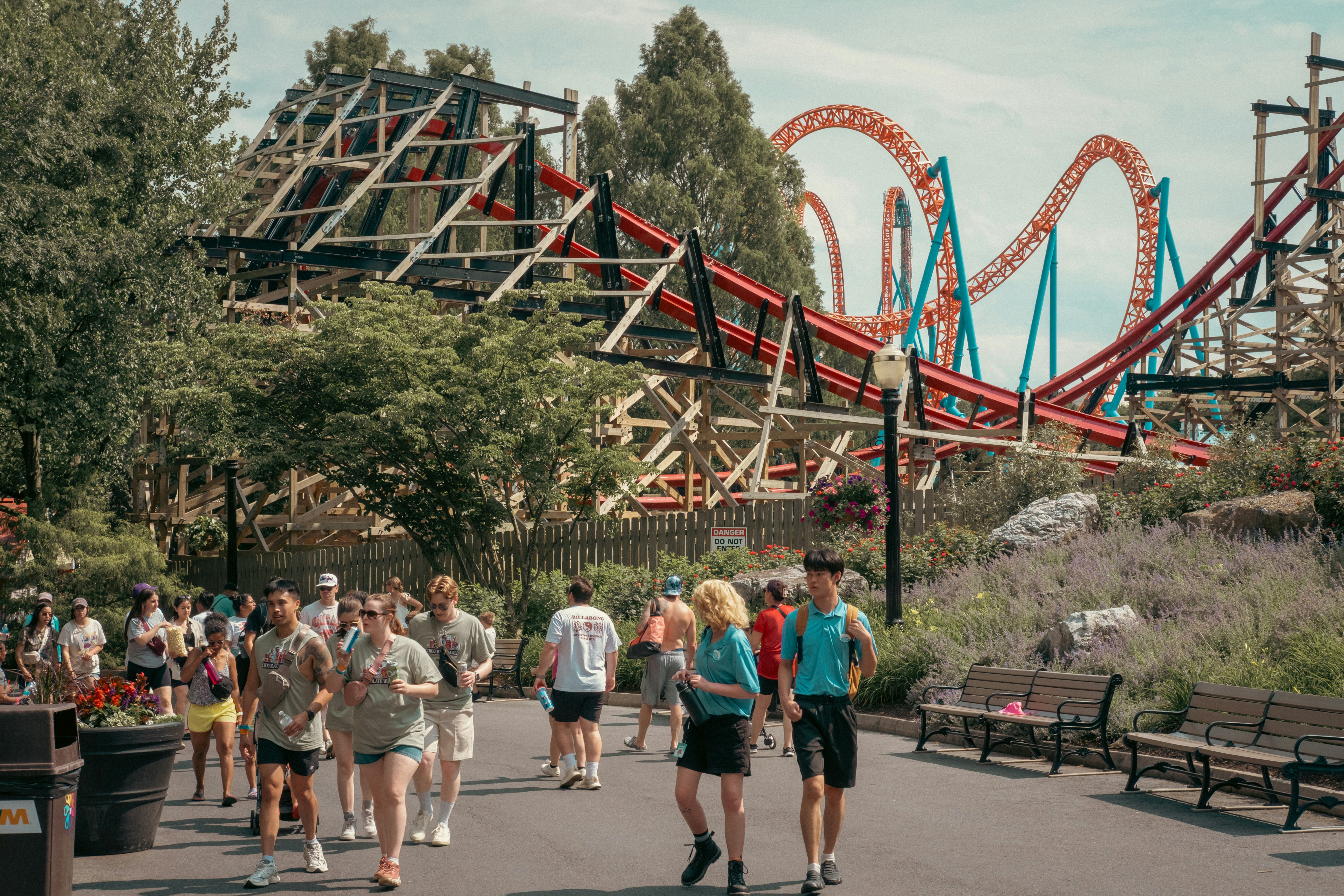 People walk past thrilling roller coasters in an amusement park.