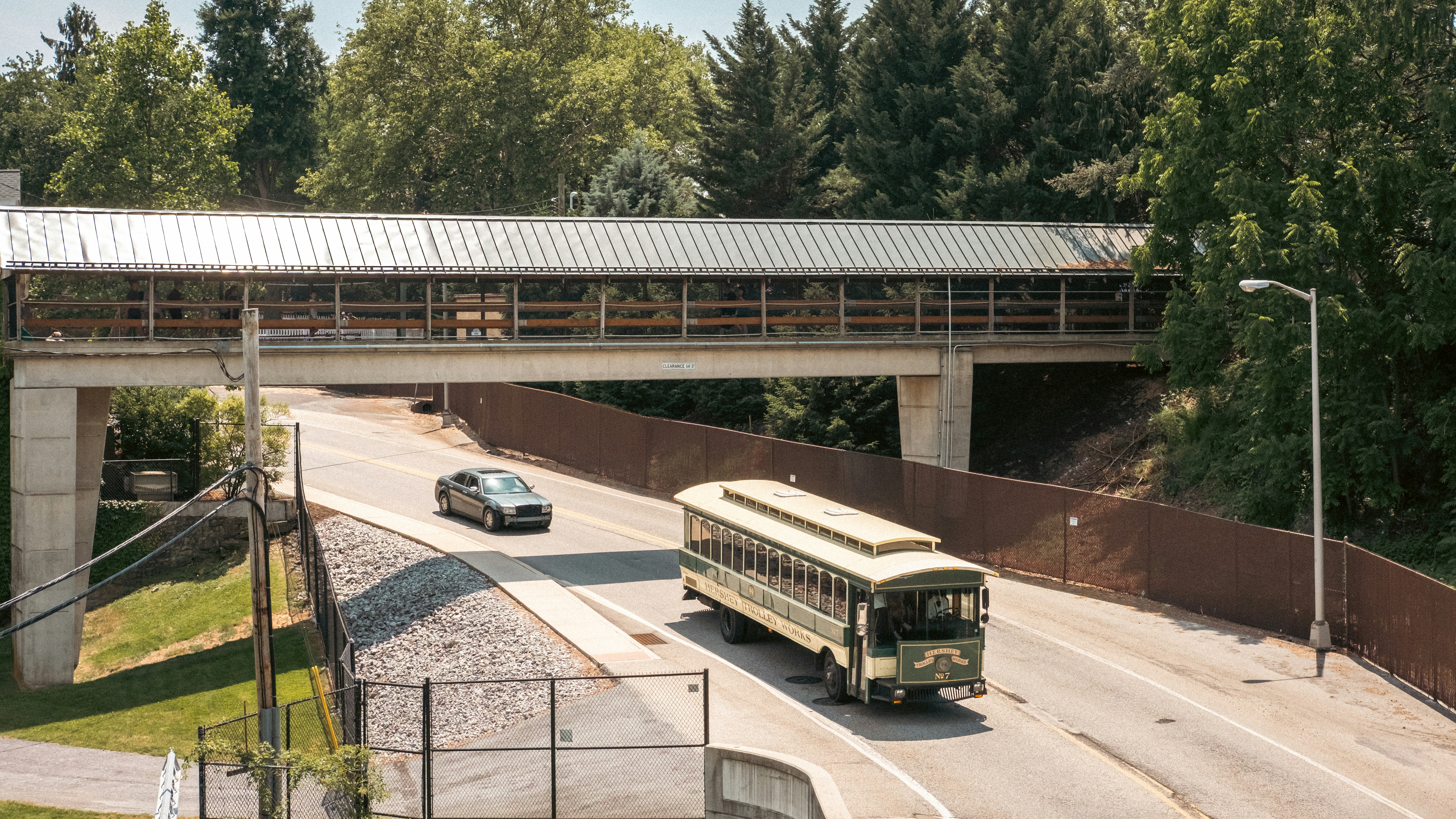 A trolley bus and car pass under a pedestrian skywalk.
