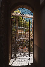 Intricate metal gate at archway's end, revealing sunny landscape.
