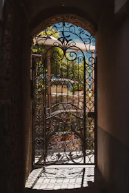 Intricate metal gate at archway's end, revealing sunny landscape.