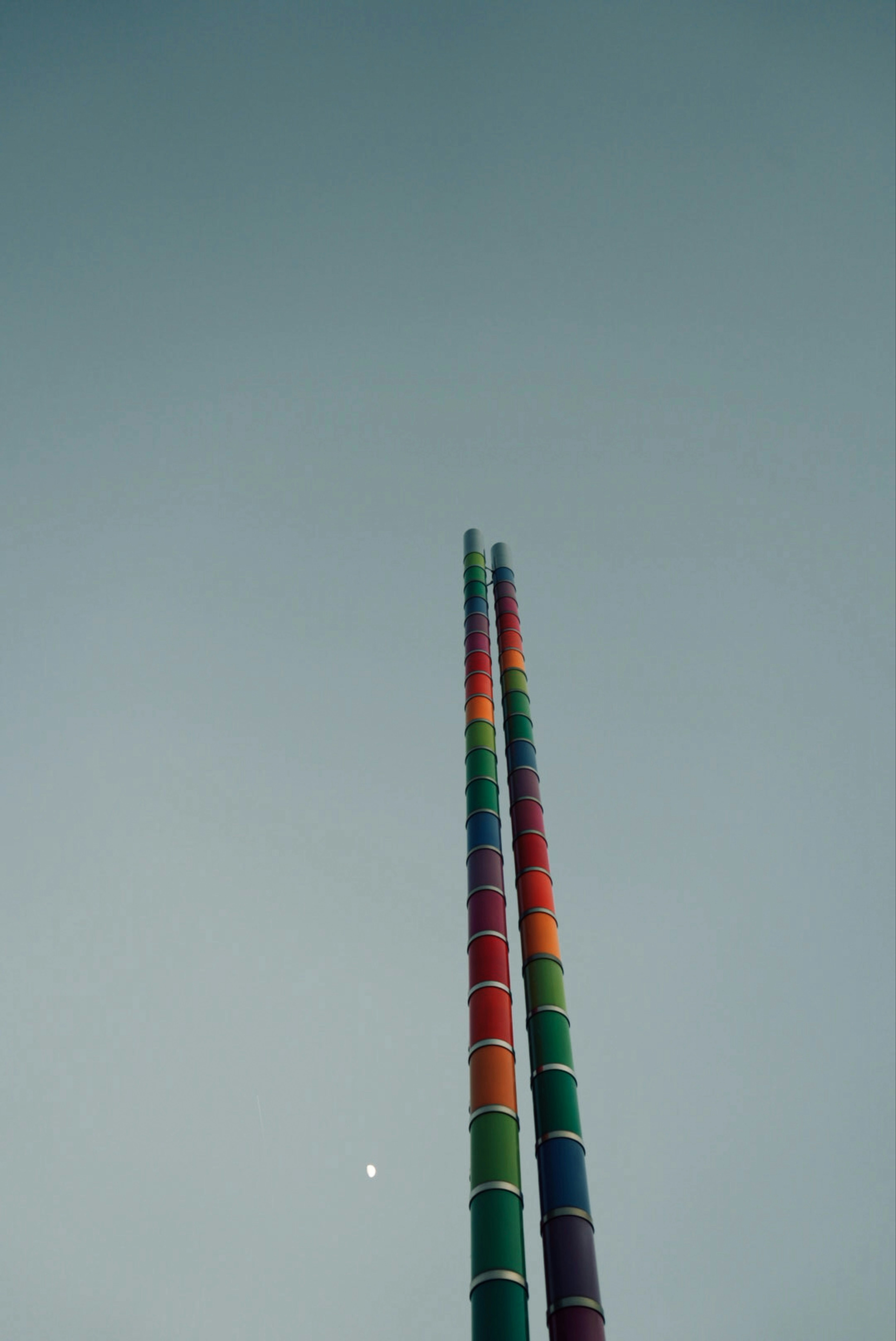 Two colorful rainbow-striped poles stand against a clear blue sky.