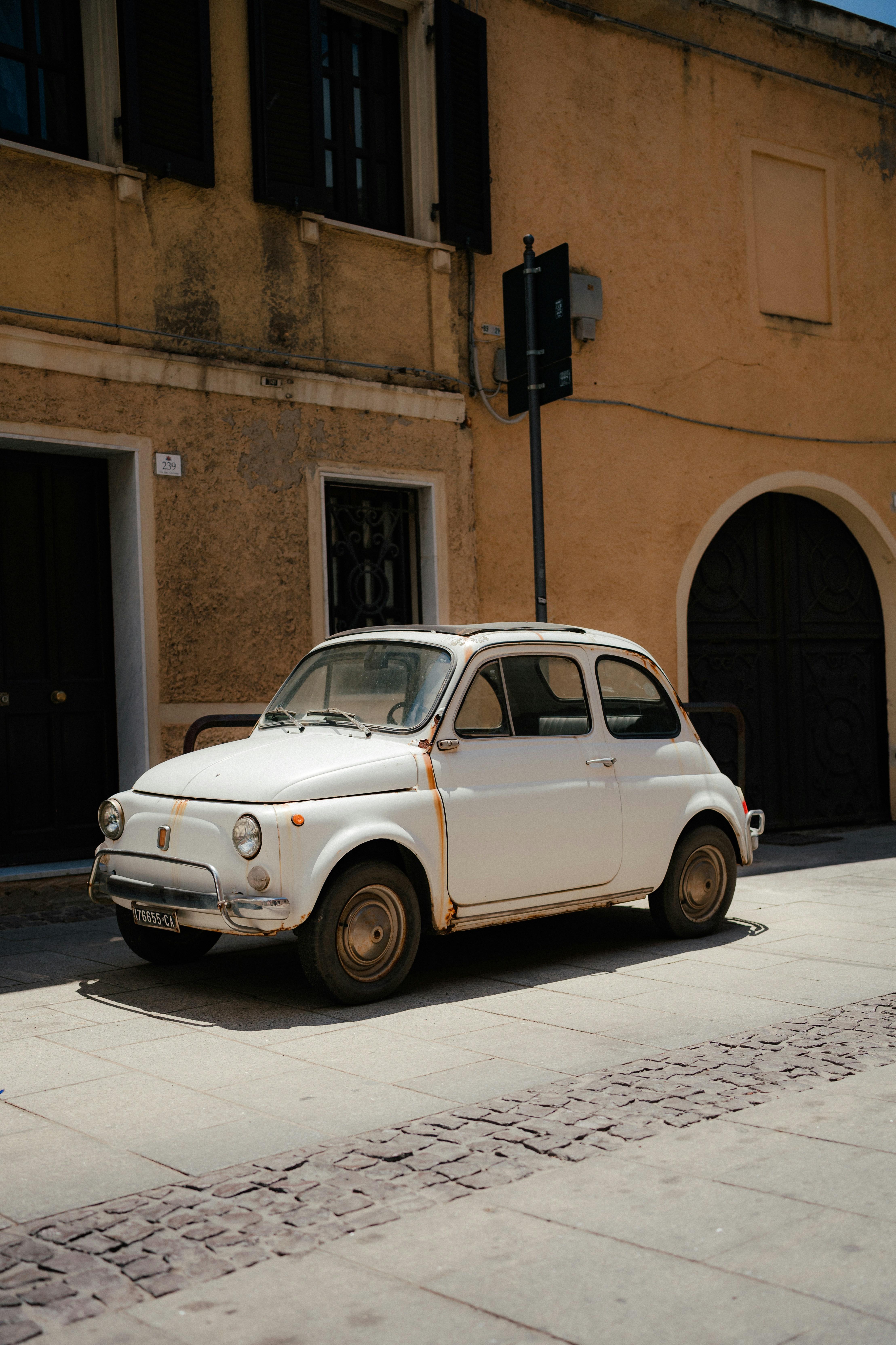 A rusty white vintage car parked on a sunny street.