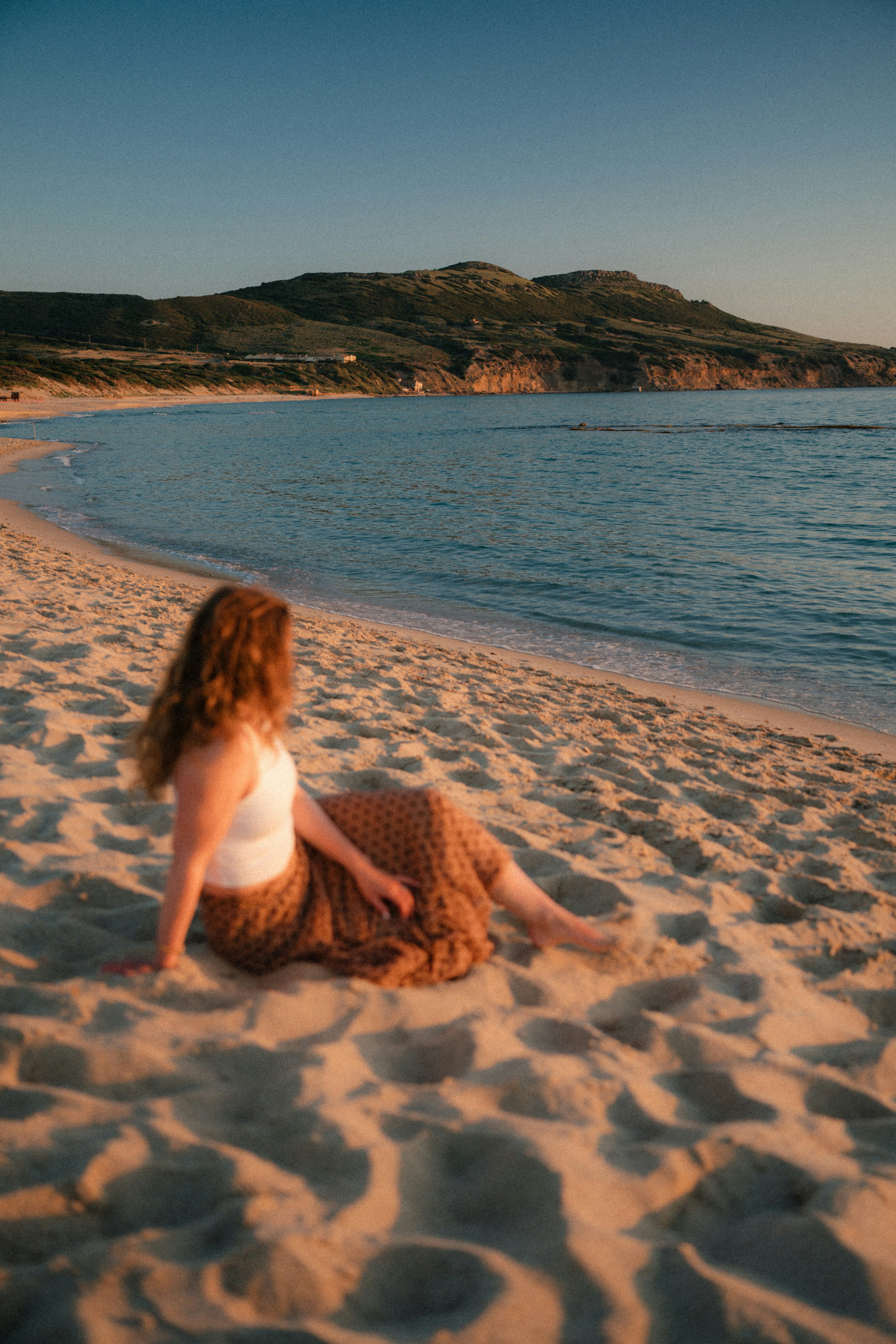 Woman sitting on a sandy beach looking at the ocean.