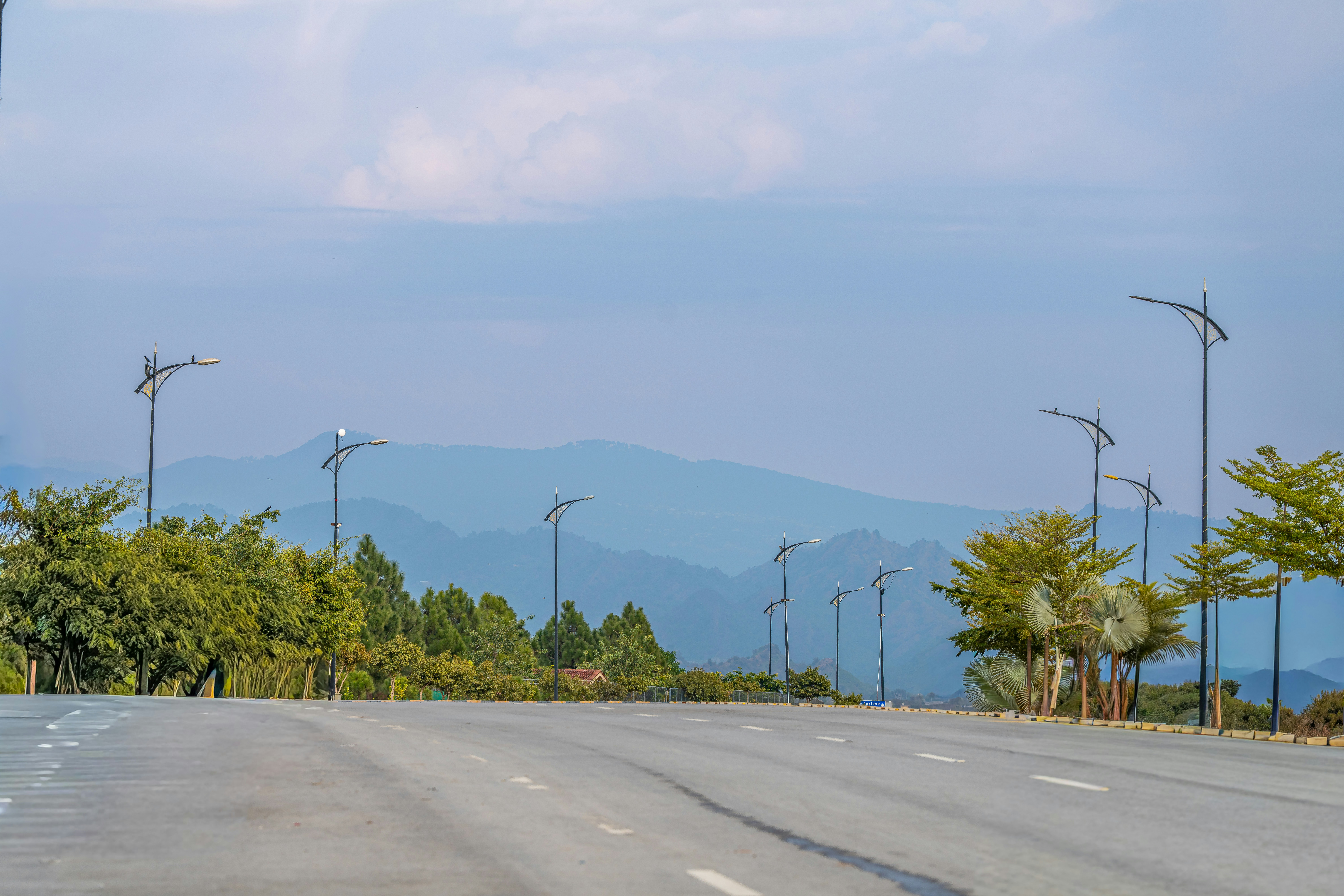 Empty road leading towards distant mountains and green trees.