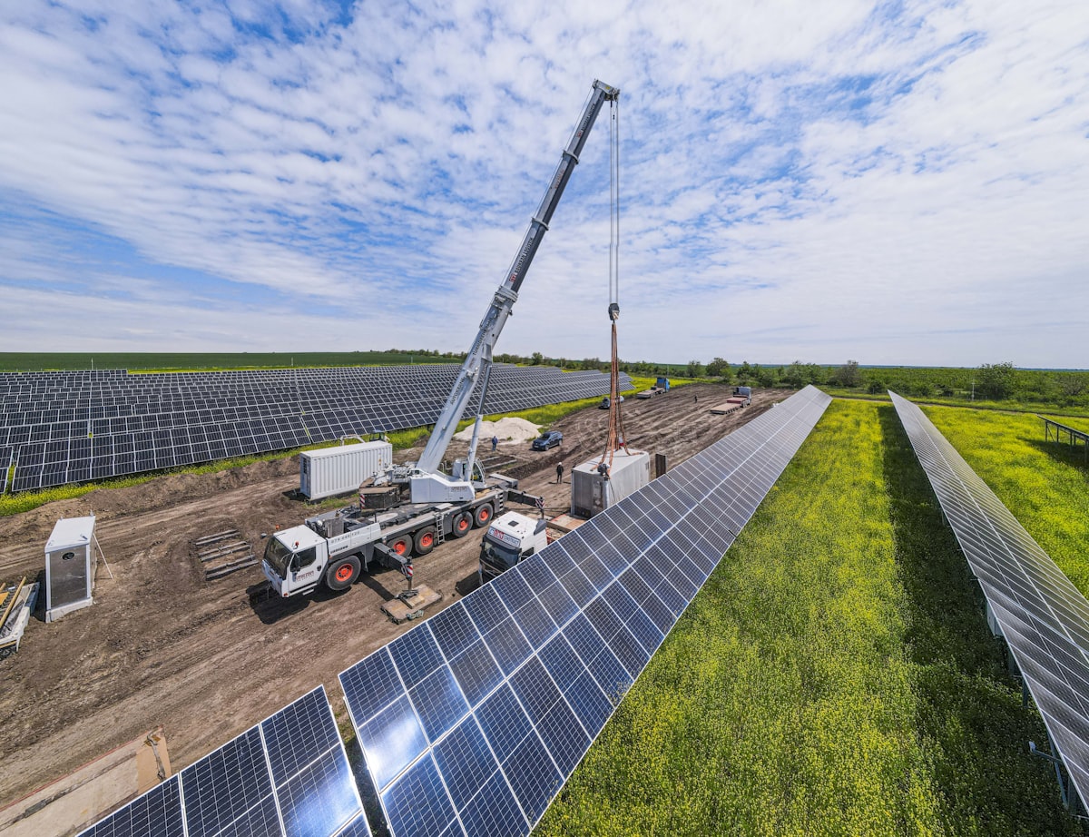 A construction crane working at a large utility-scale solar panel farm, standing in for the physical-work-of-significant-nature activity Notice 2025-42 now requires as the sole route to begin-of-construction status for solar facilities above 1.5 MWac and for all wind facilities under Sections 45Y and 48E after the July 4, 2026 OBBBA deadline.