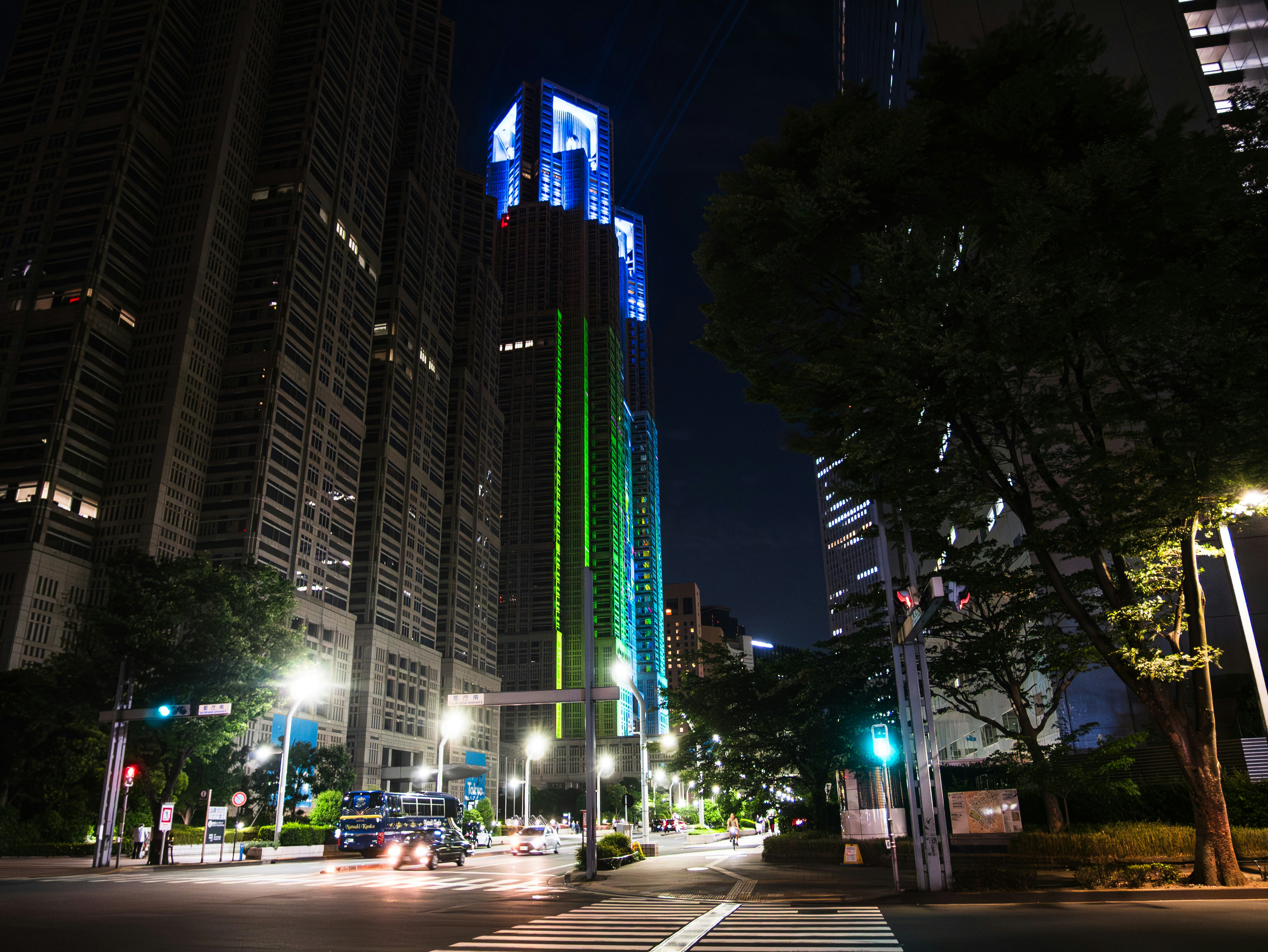 Cityscape at night with illuminated skyscrapers, streets, and trees