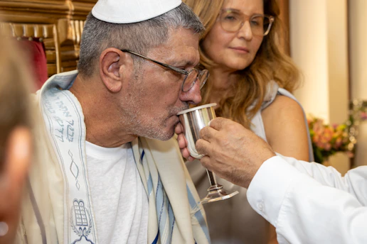 Man in kippah and tallit drinks from a silver cup