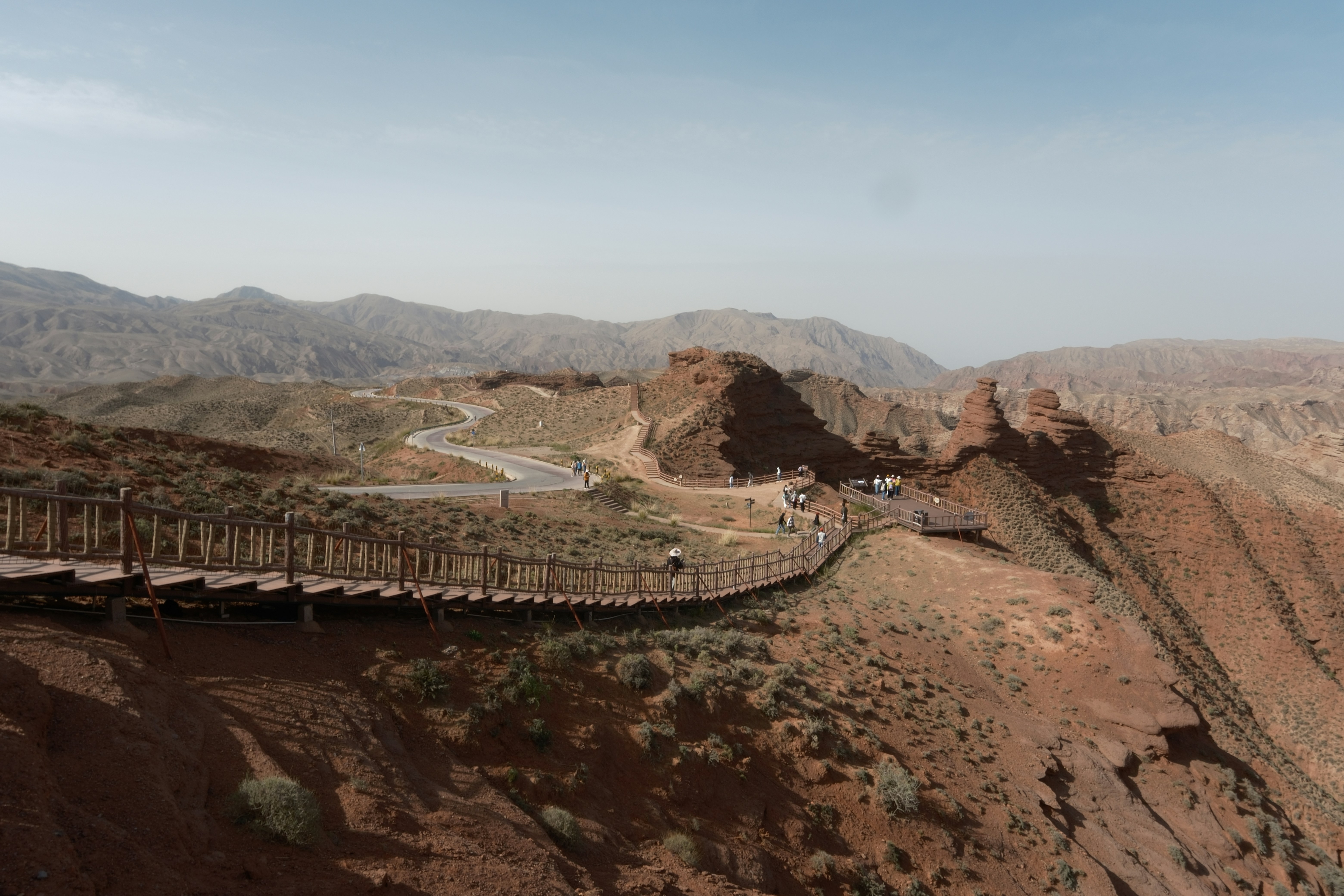 Wooden walkway and road in a vast desert mountain landscape.