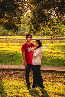 Two young people holding badminton rackets in a sunny park.