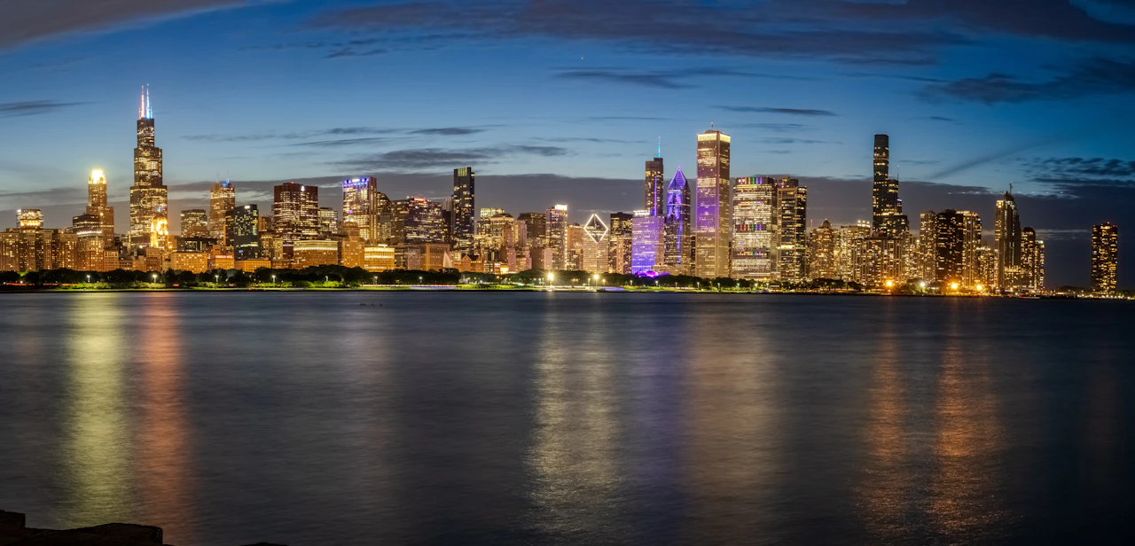 Bright city lights reflect on water under a twilight sky