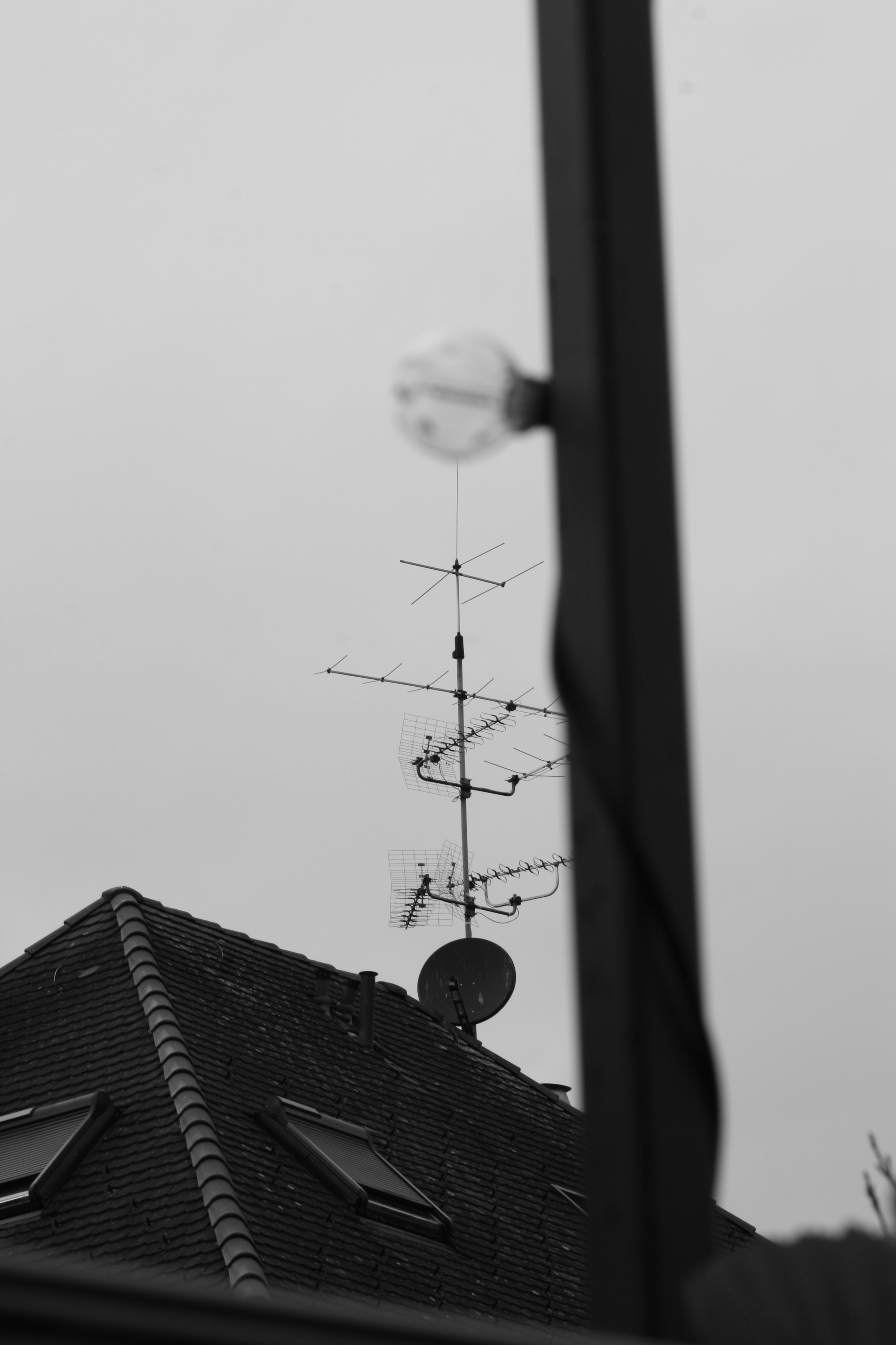 Tetto in scala di grigi con antenne sotto un cielo nuvoloso.