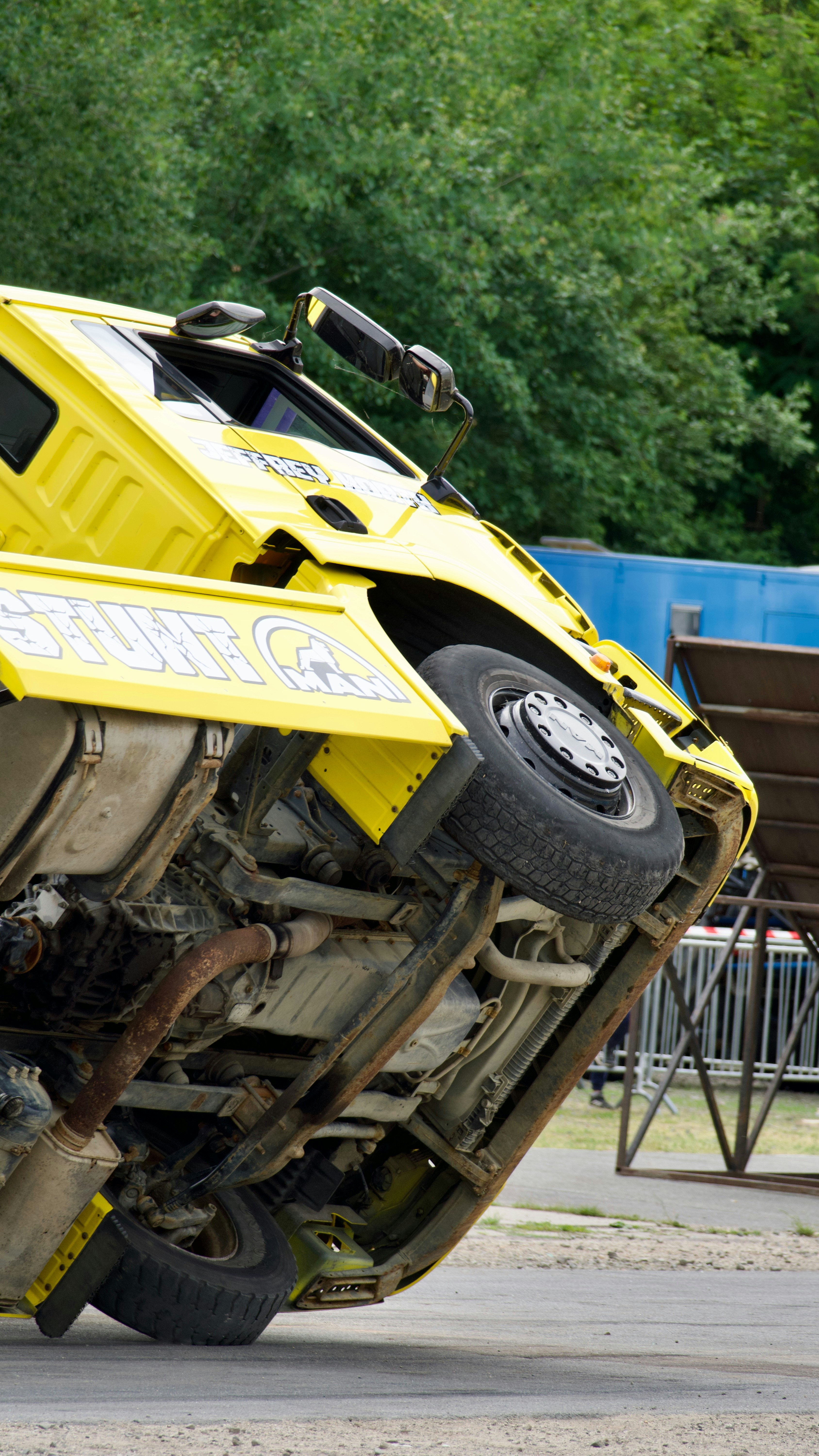 Yellow truck performing a two-wheel stunt on asphalt.