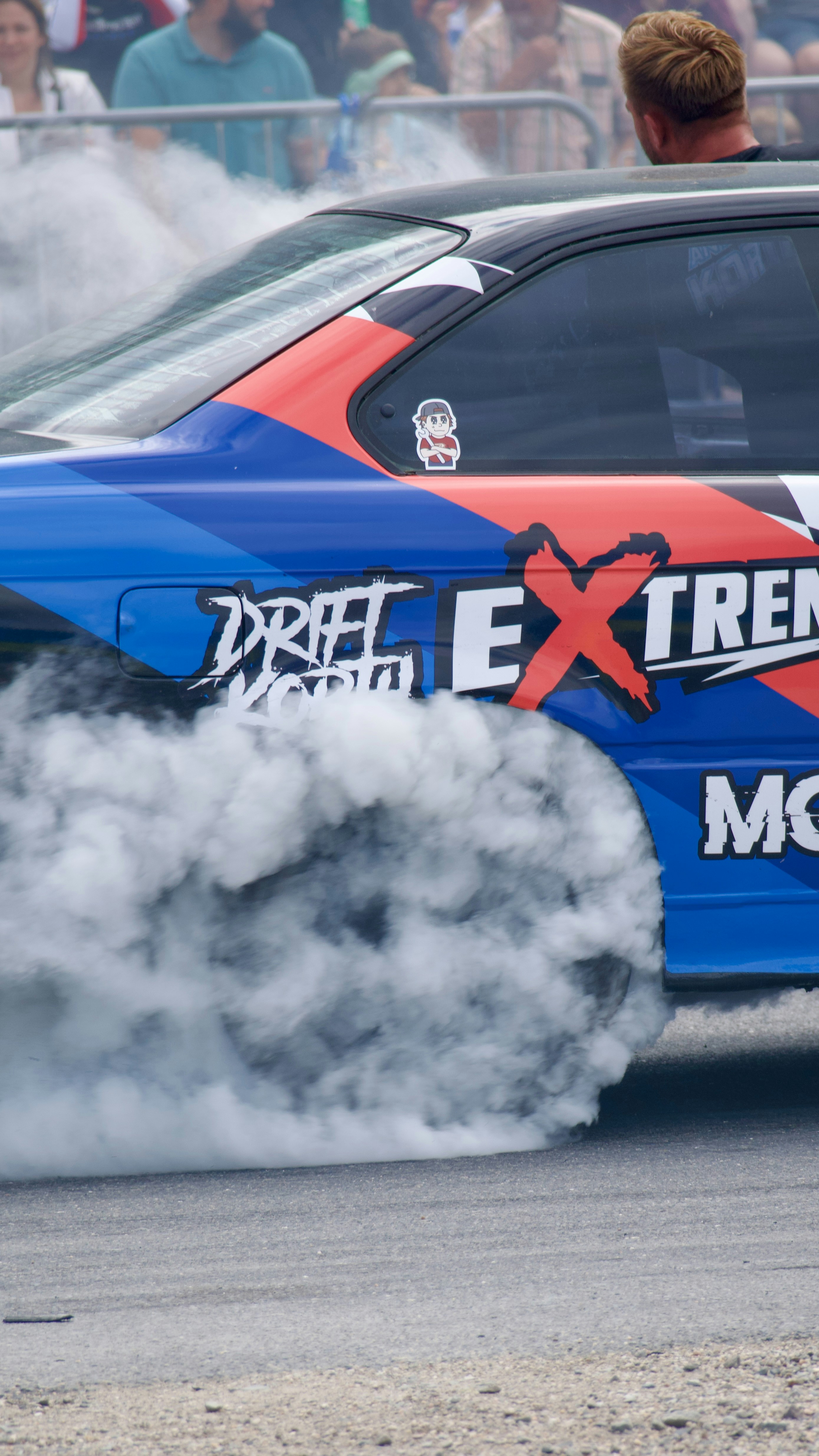 A blue race car drifts, creating thick tire smoke.