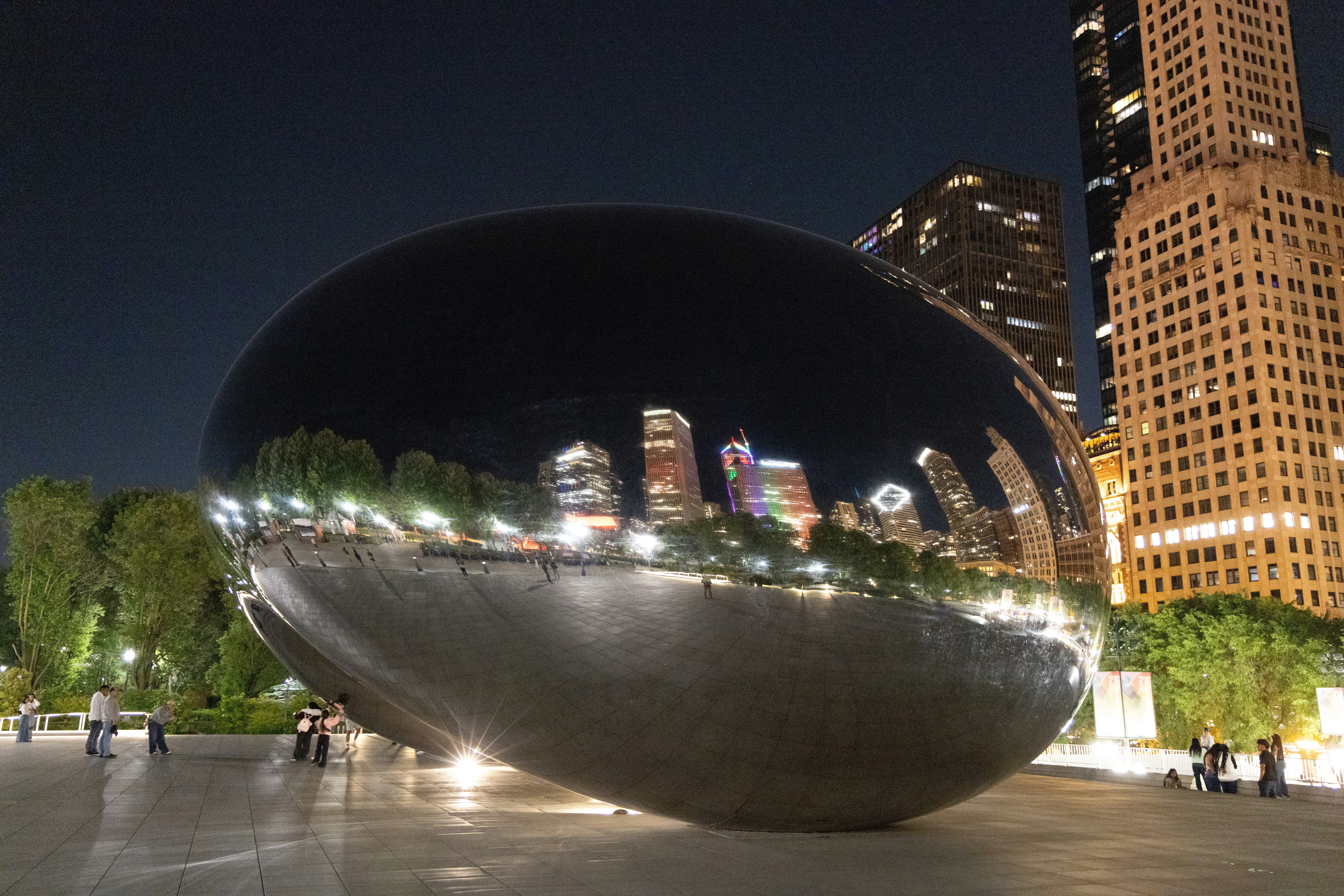 Cloud gate sculpture reflecting chicago skyline at night.