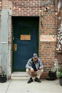 Older man sits on a doorstep, checking his phone