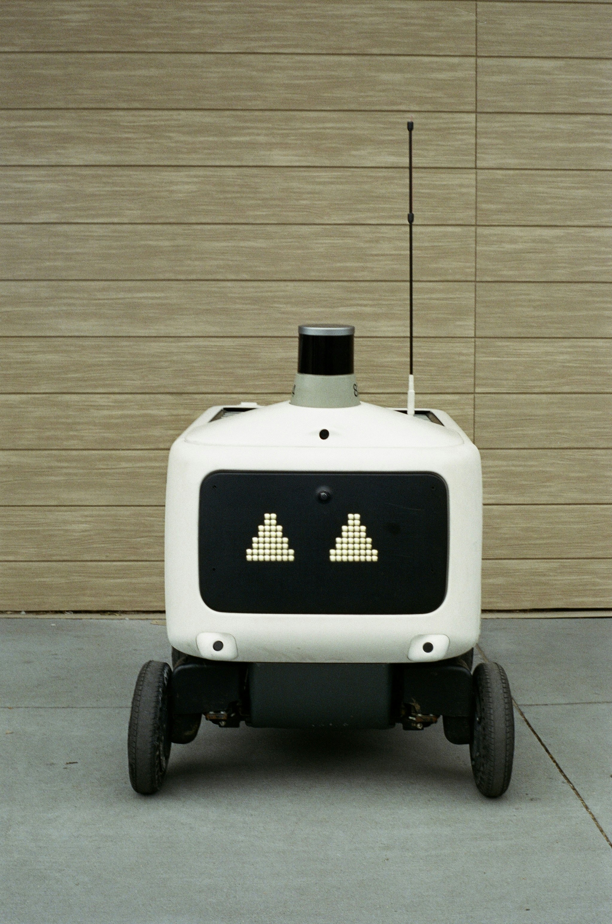 A white delivery robot with digital eyes and an antenna.