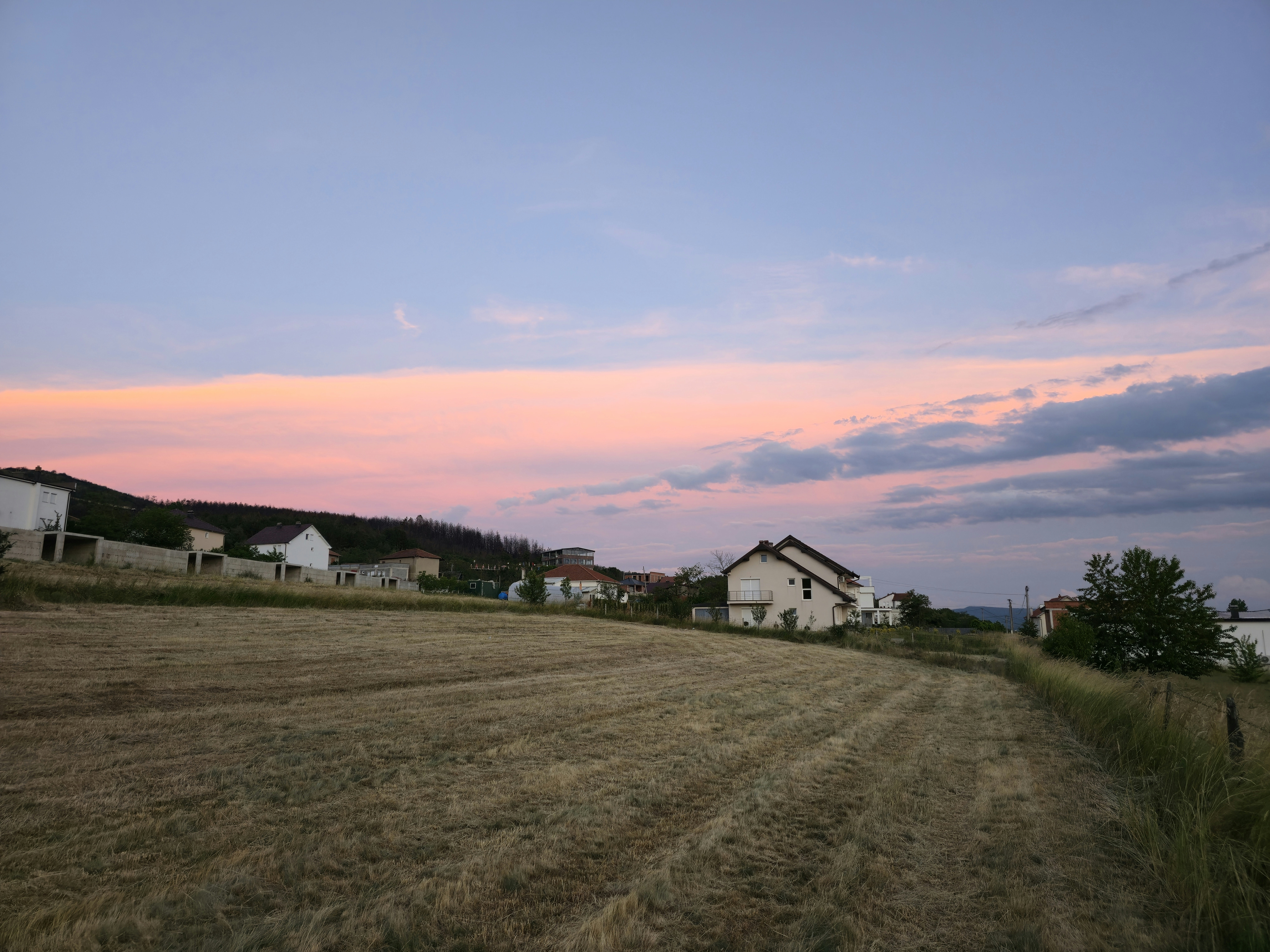 Rural village at sunset with a field and colorful sky.