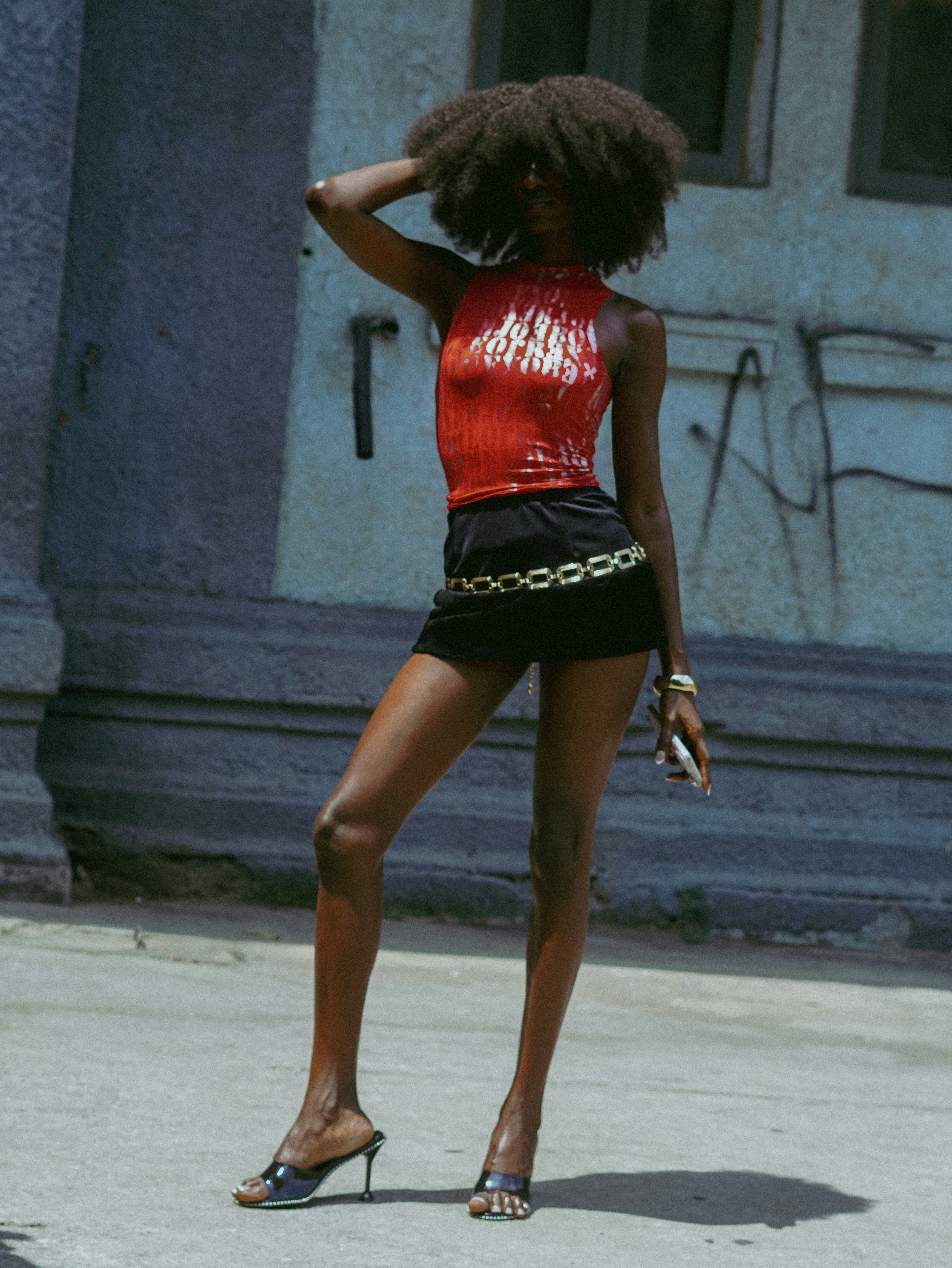 Fashionable woman in red top and black shorts posing outside.