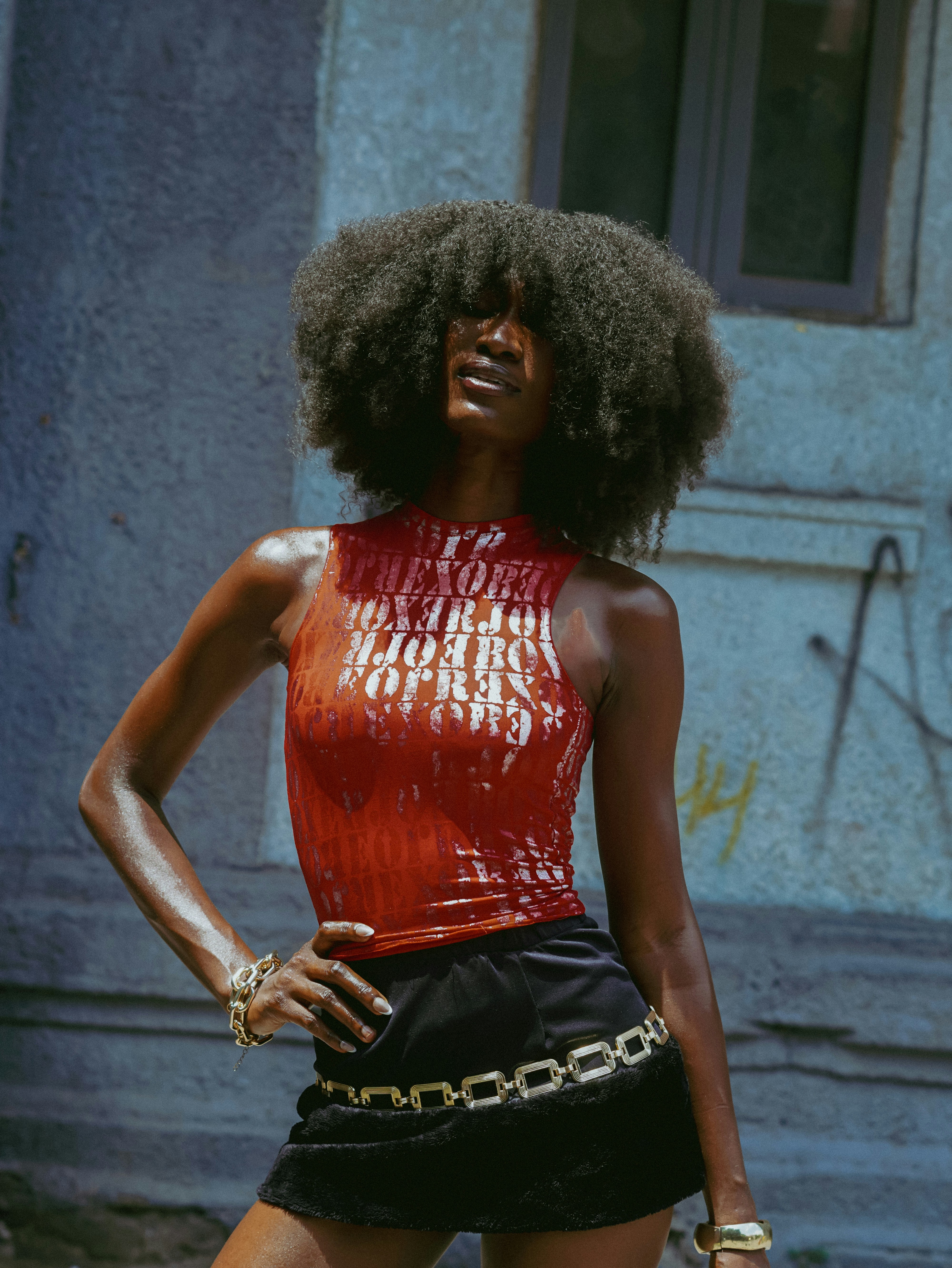 Dark-skinned woman with afro hair, red top, and black skirt.