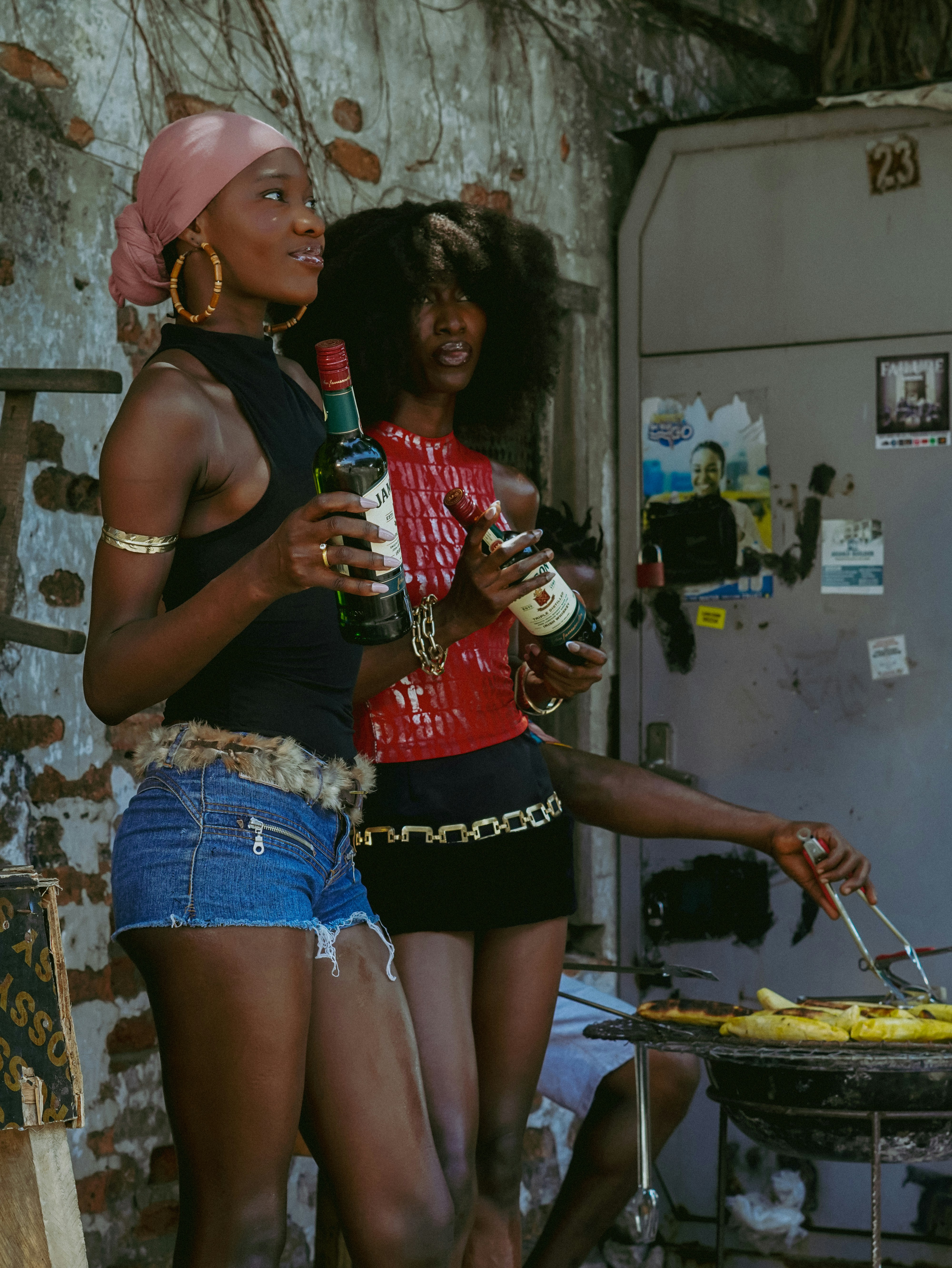 Two women hold bottles while another person grills food.