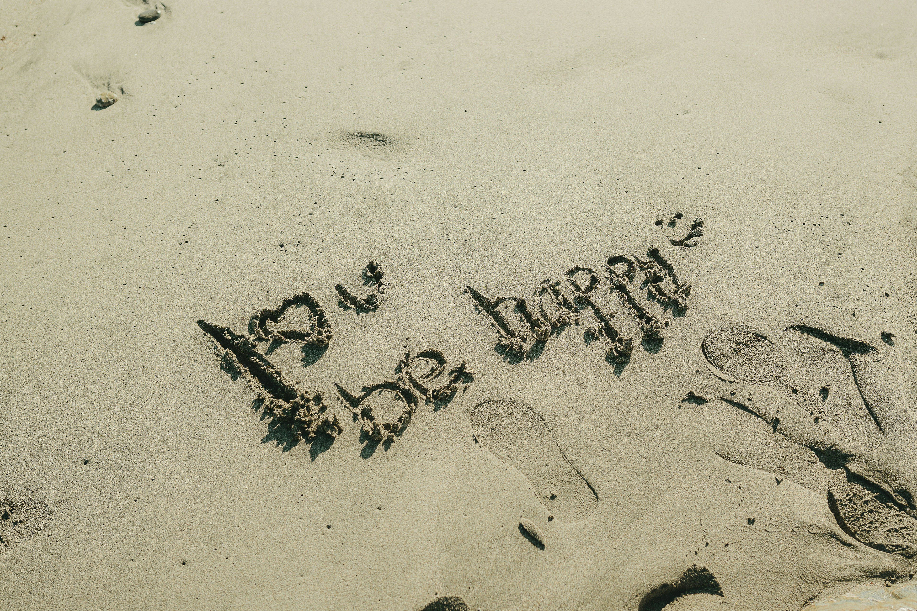 The words 'be happy' written in sand with footprints.