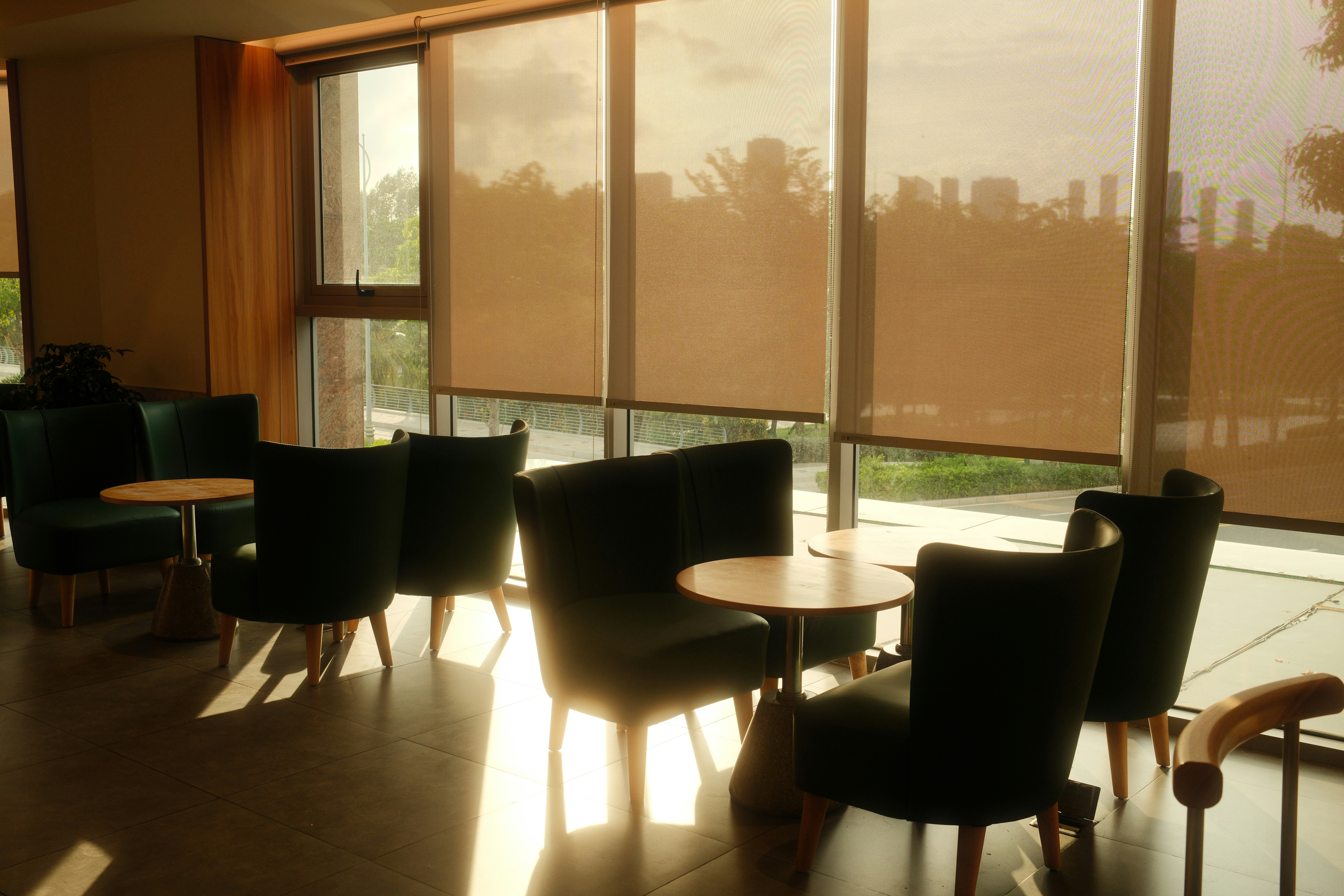 Sunlit lounge area with chairs, tables, and window blinds.