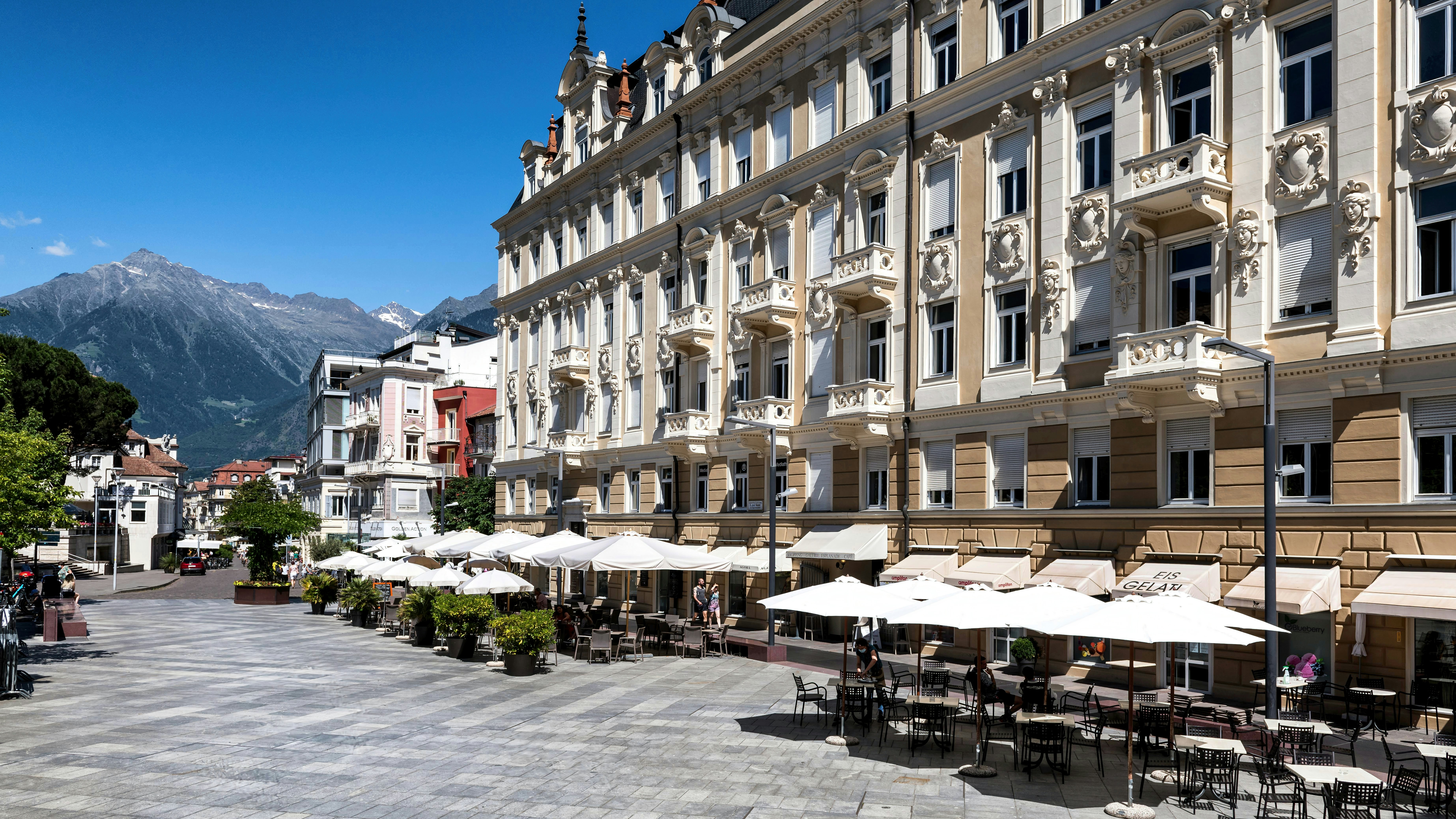 Ornate building facade overlooks outdoor cafe with mountains in background.