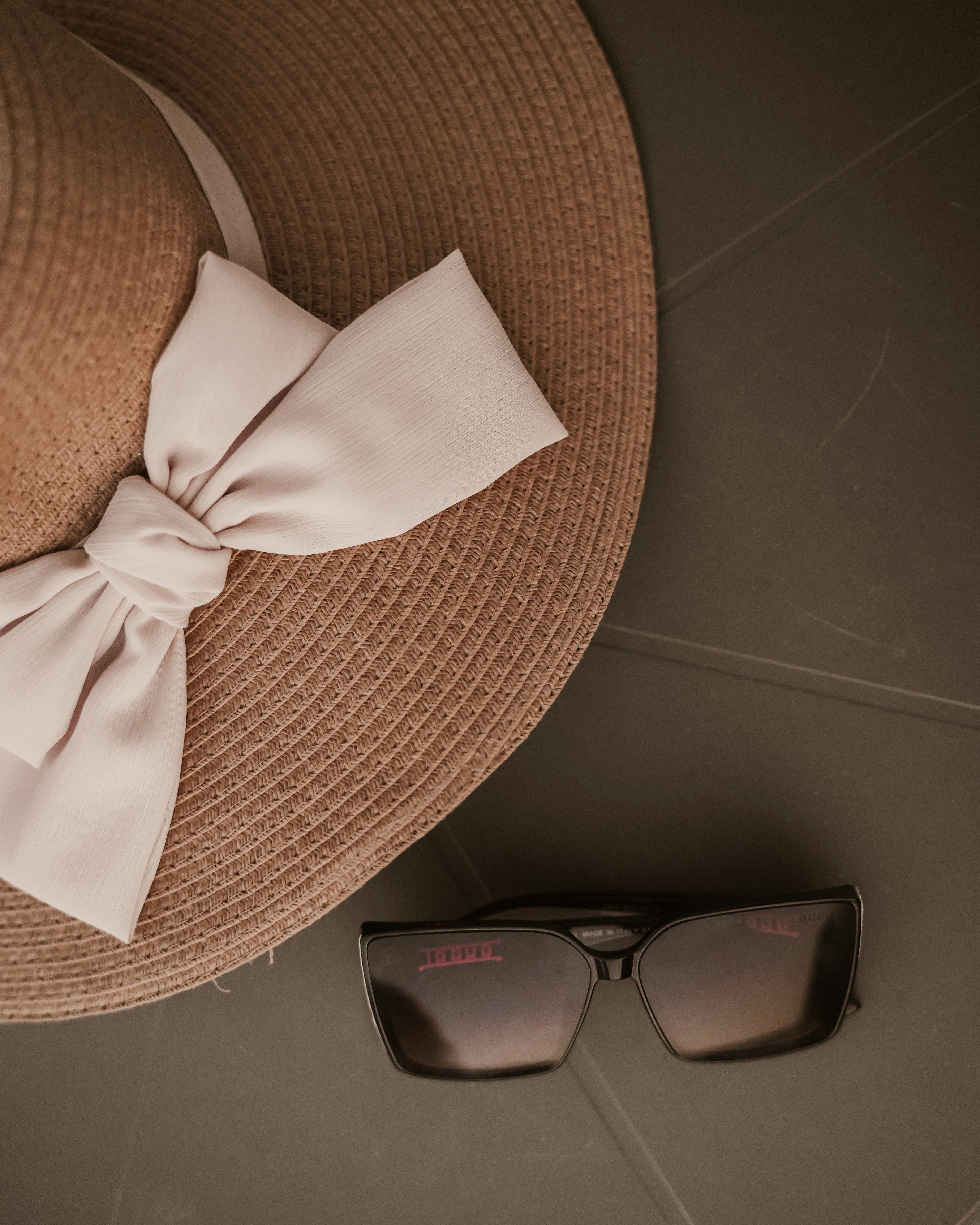 Elegant straw hat and dark sunglasses on a grey surface.