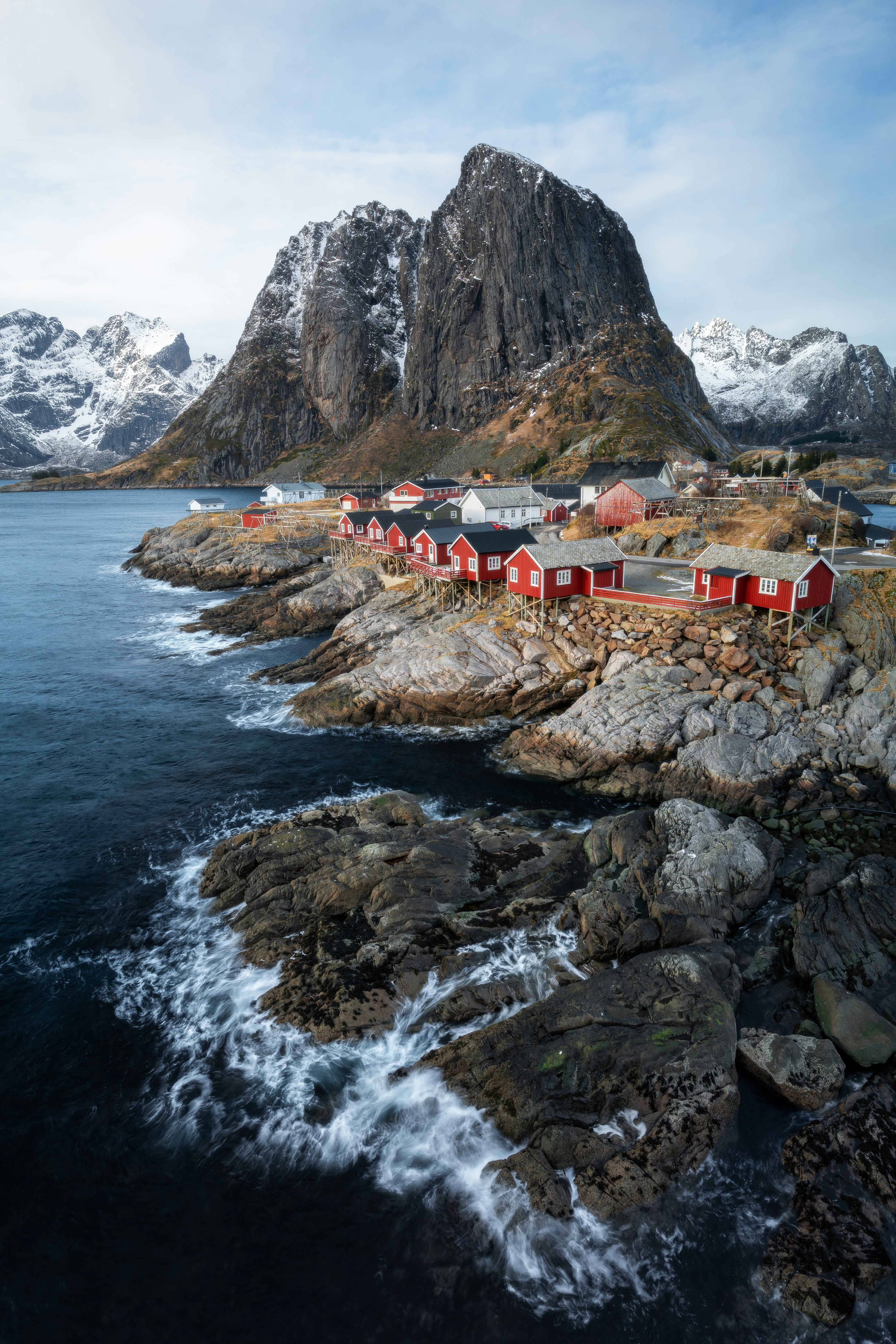 Red houses line a rocky coast with snow-capped mountains.