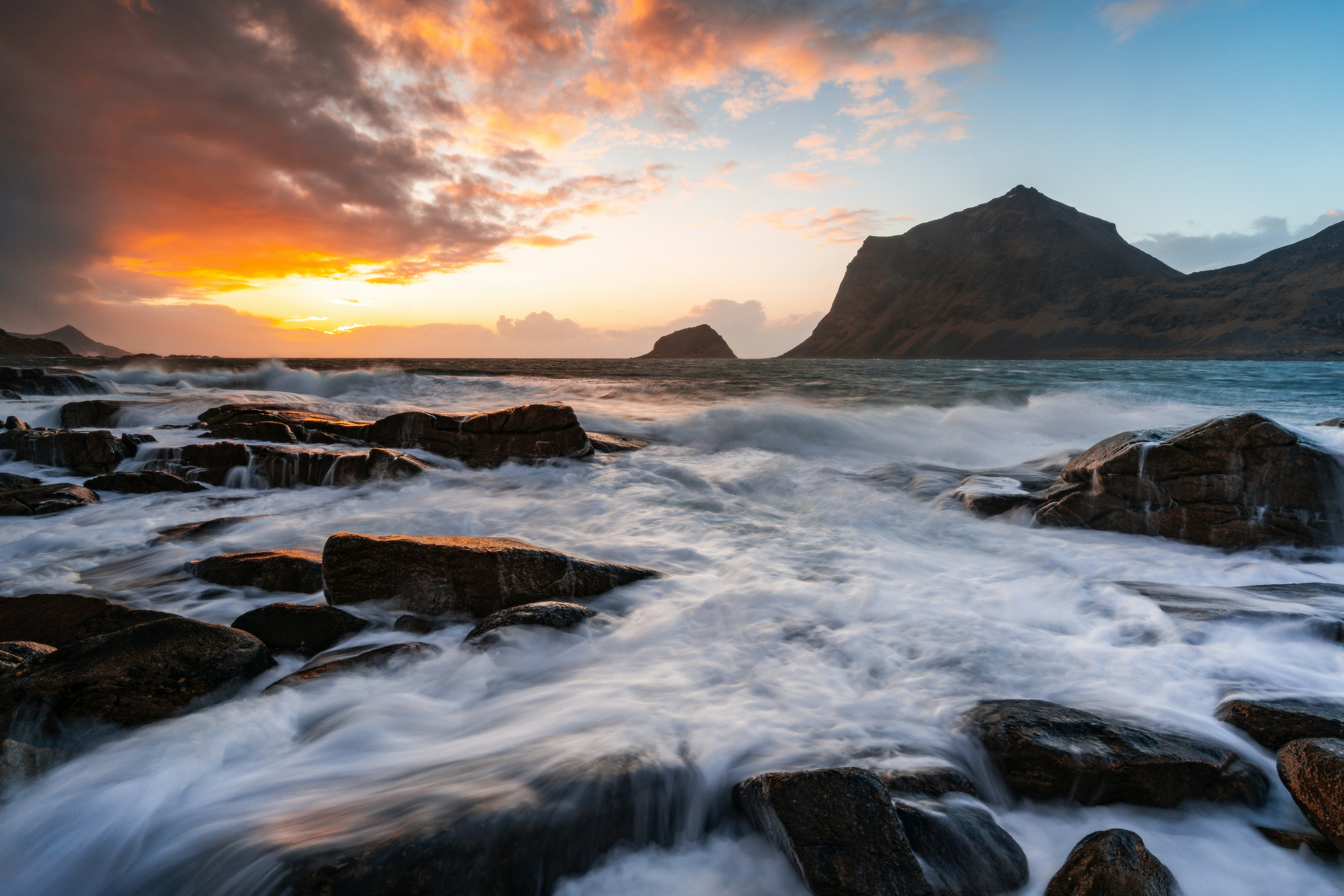 Vibrant sunset illuminates ocean waves crashing on a rocky shore.