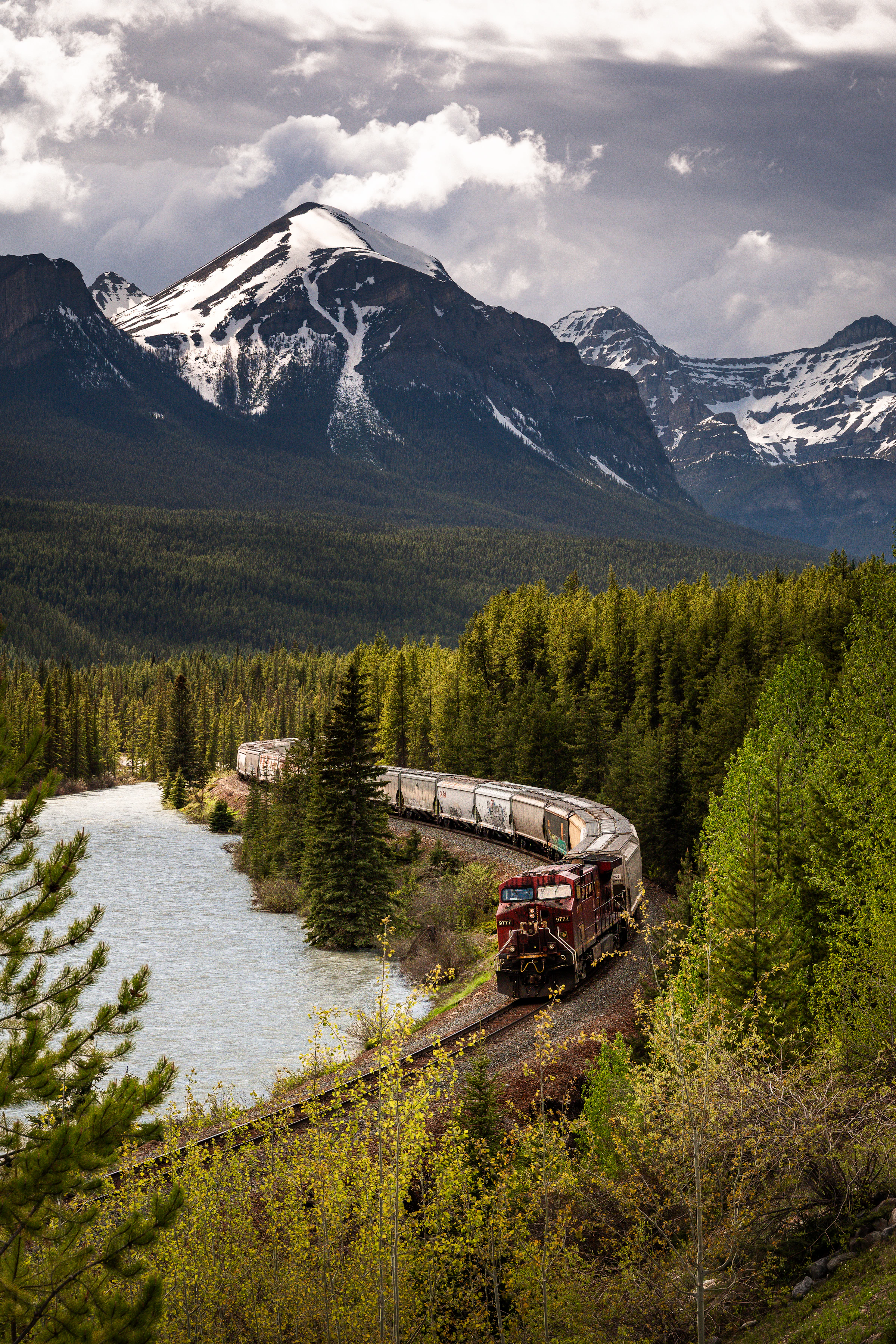 A Canadian Pacific freight train curving along a river through the Rocky Mountains