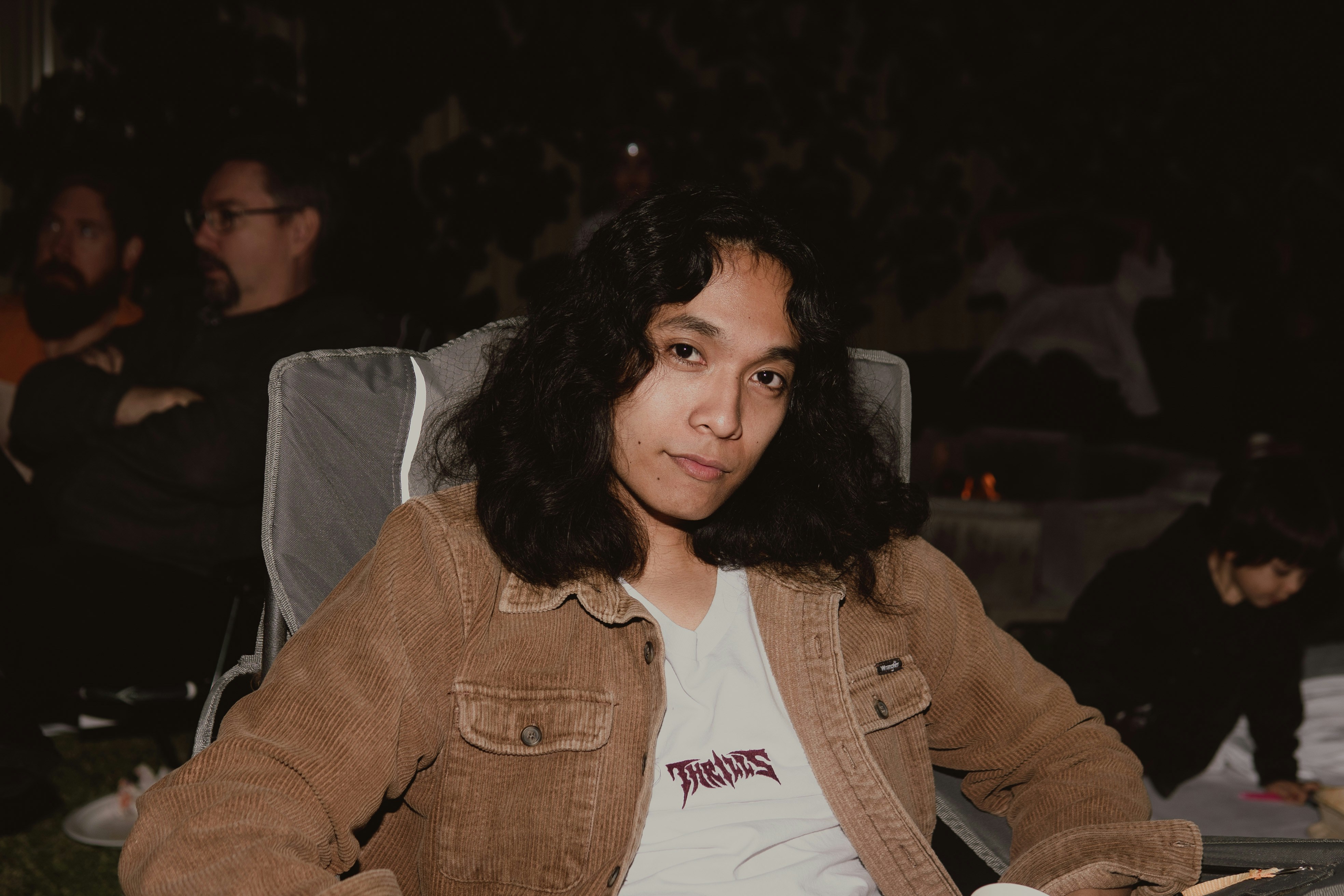 Young man with long hair sitting outdoors at night.