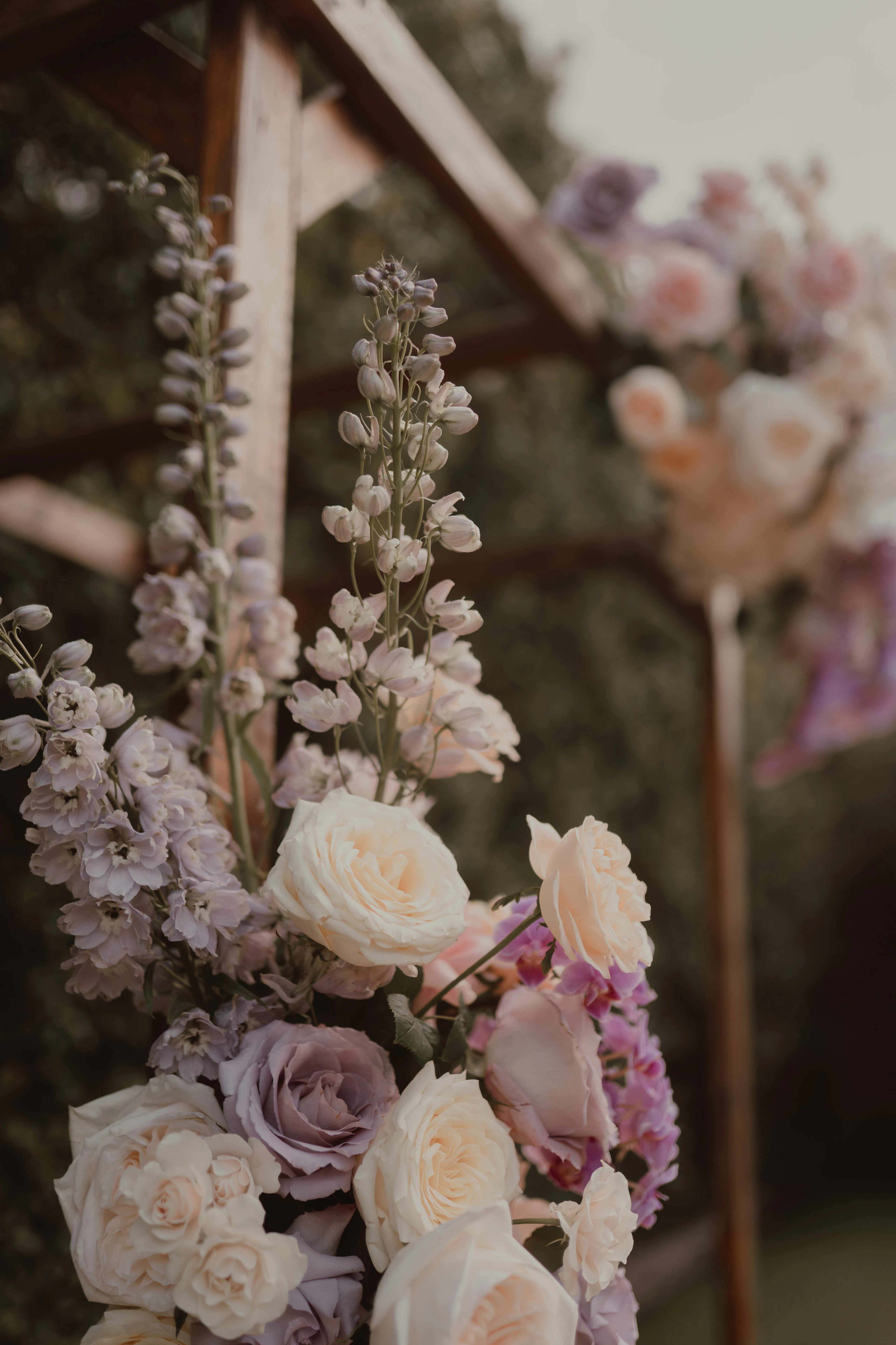 A floral installation of cream roses, lilac roses and pale delphinium on a wooden ceremony arch.