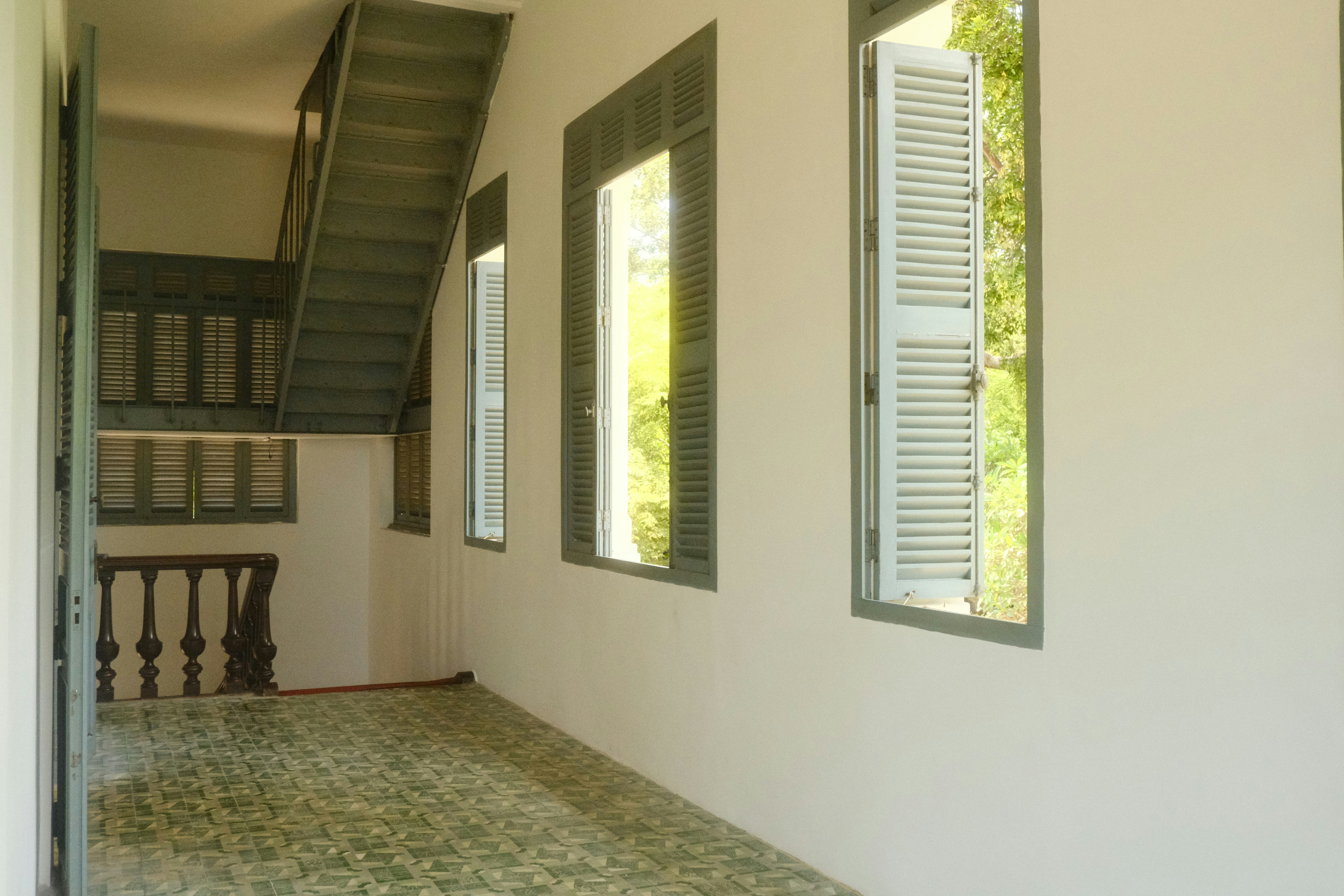 A hallway with windows, green shutters, and a staircase.