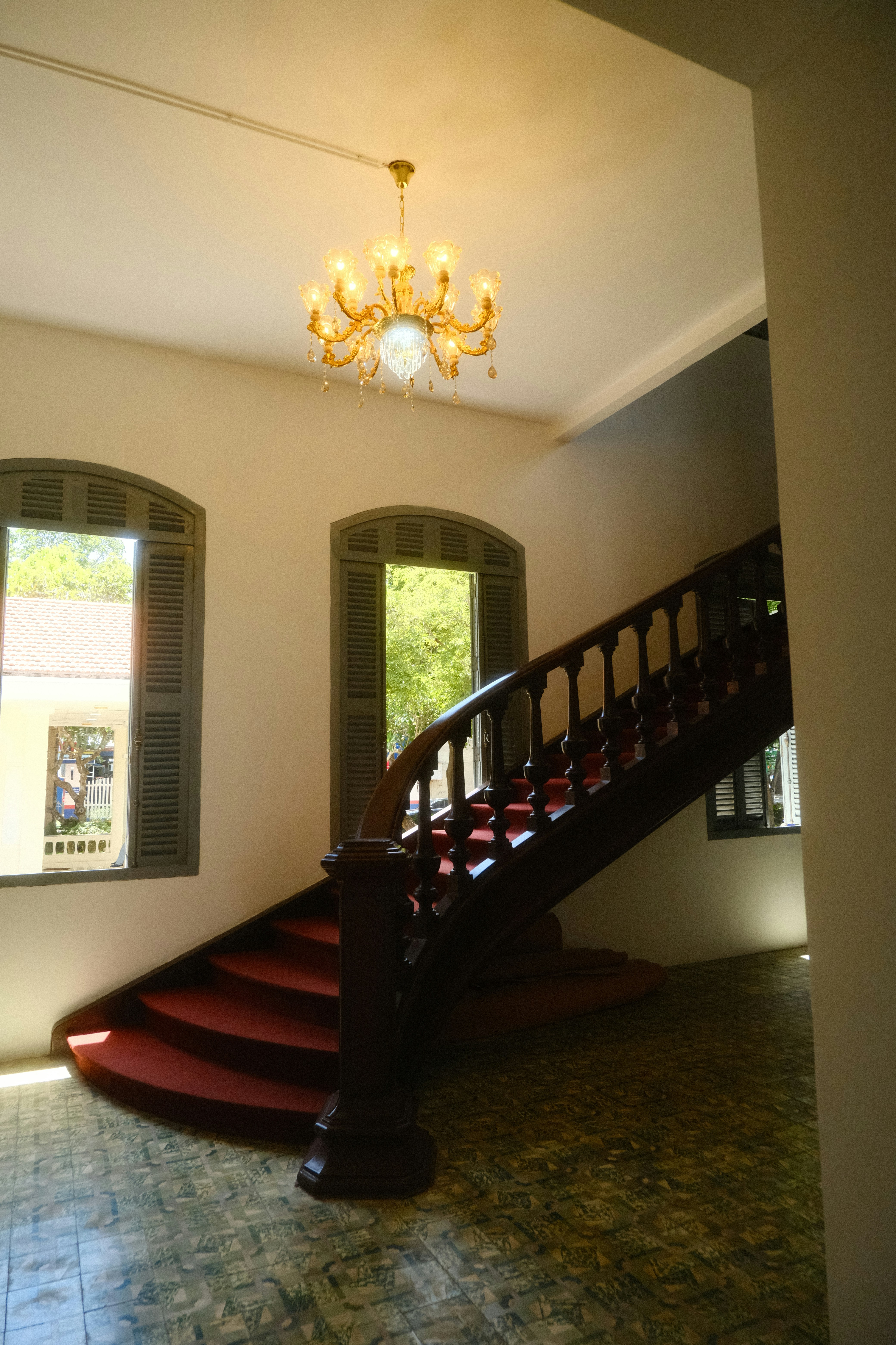A grand wooden staircase with red carpet and a chandelier.