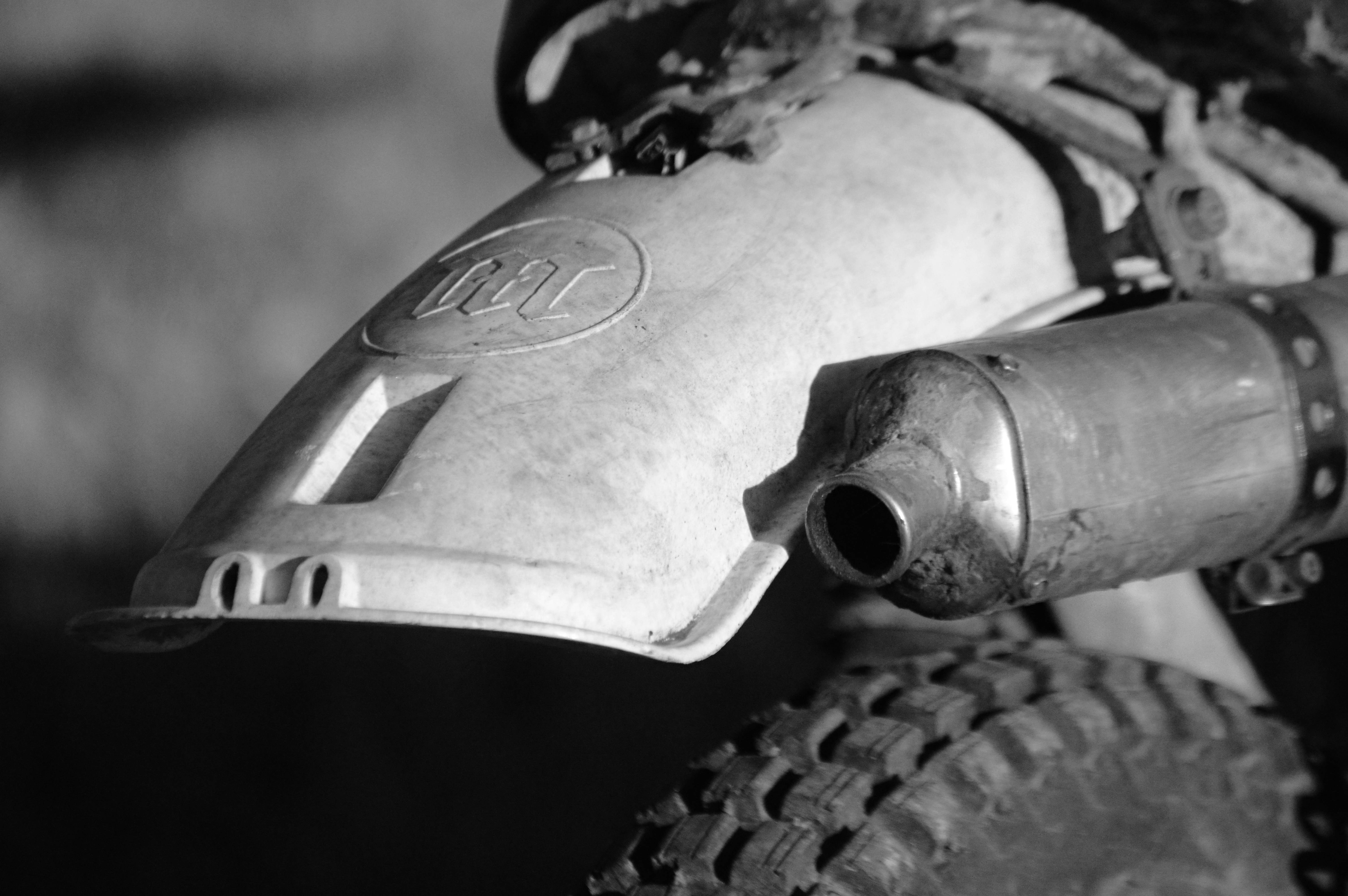 Parafango posteriore e scarico di moto da cross sporco in bianco e bianco.
