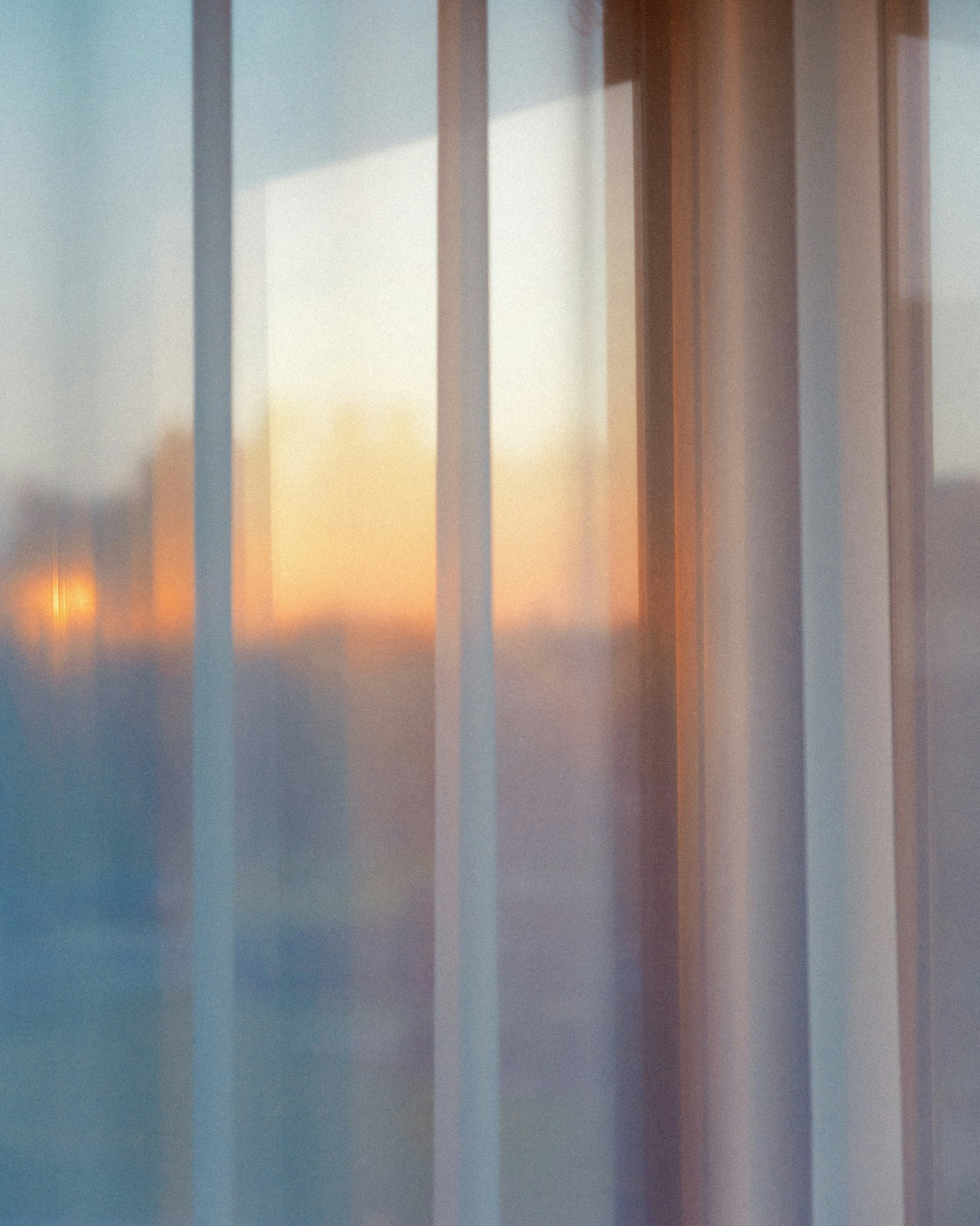 Sunset light filters through sheer curtains on a window.