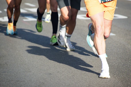 Runners' legs and feet in motion on asphalt with shadows.