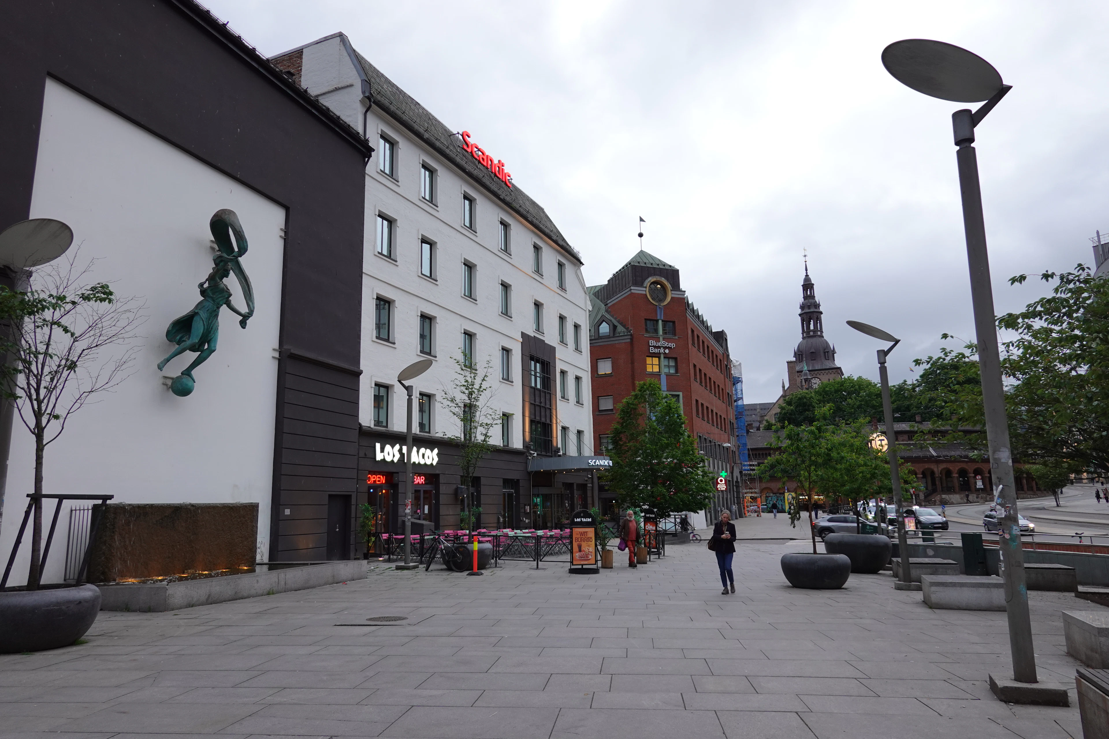 A mermaid mural on a black facade beside the brick buildings of an Oslo square