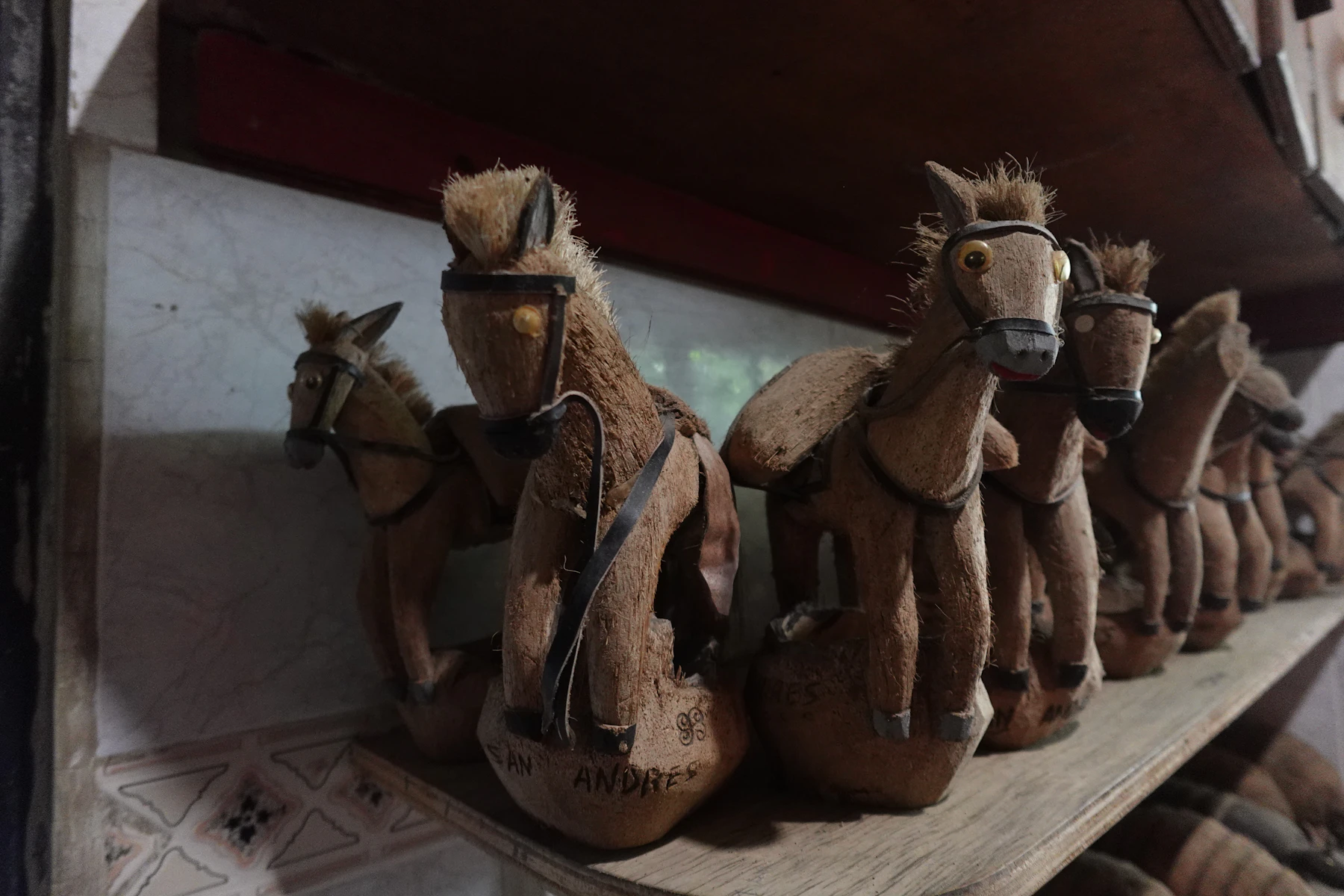 A row of handmade brown horse figures with dark bridles lined up along a wooden shelf