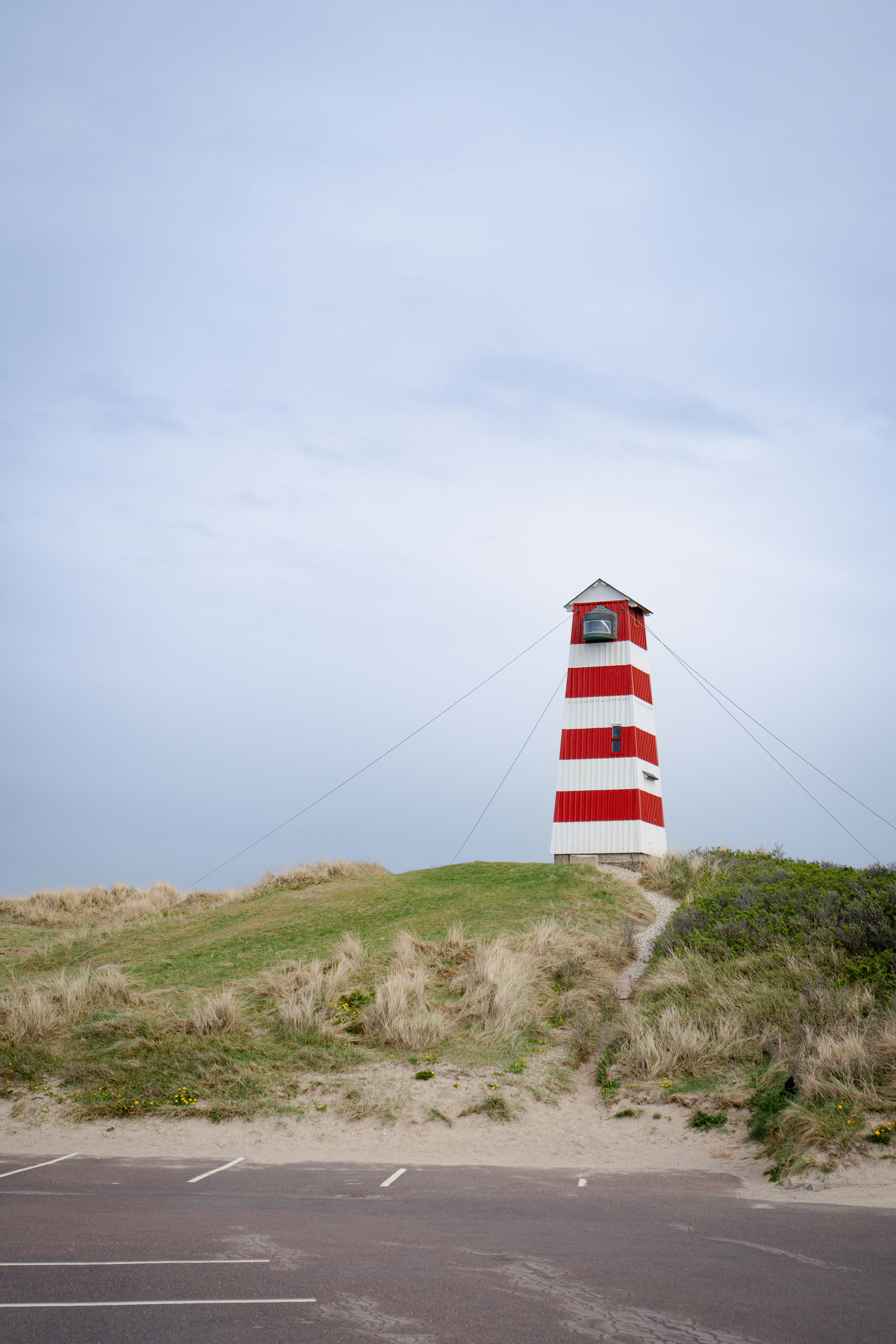 A red and white striped lighthouse on a grassy dune.