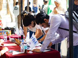 People signing documents at a red table with flags