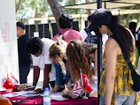 People signing papers at an outdoor table with flags.