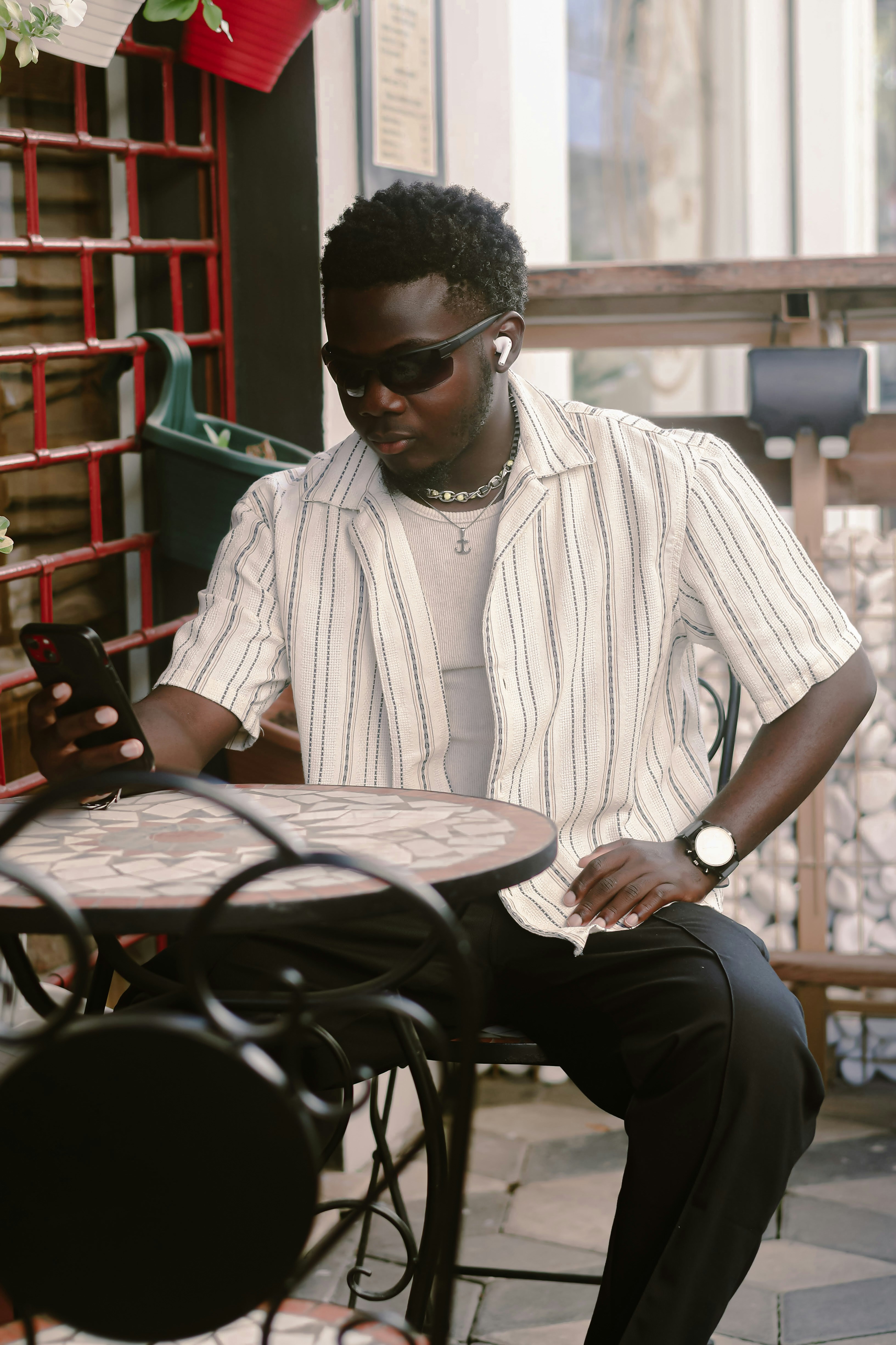 Young man with sunglasses and earbuds using phone at cafe.