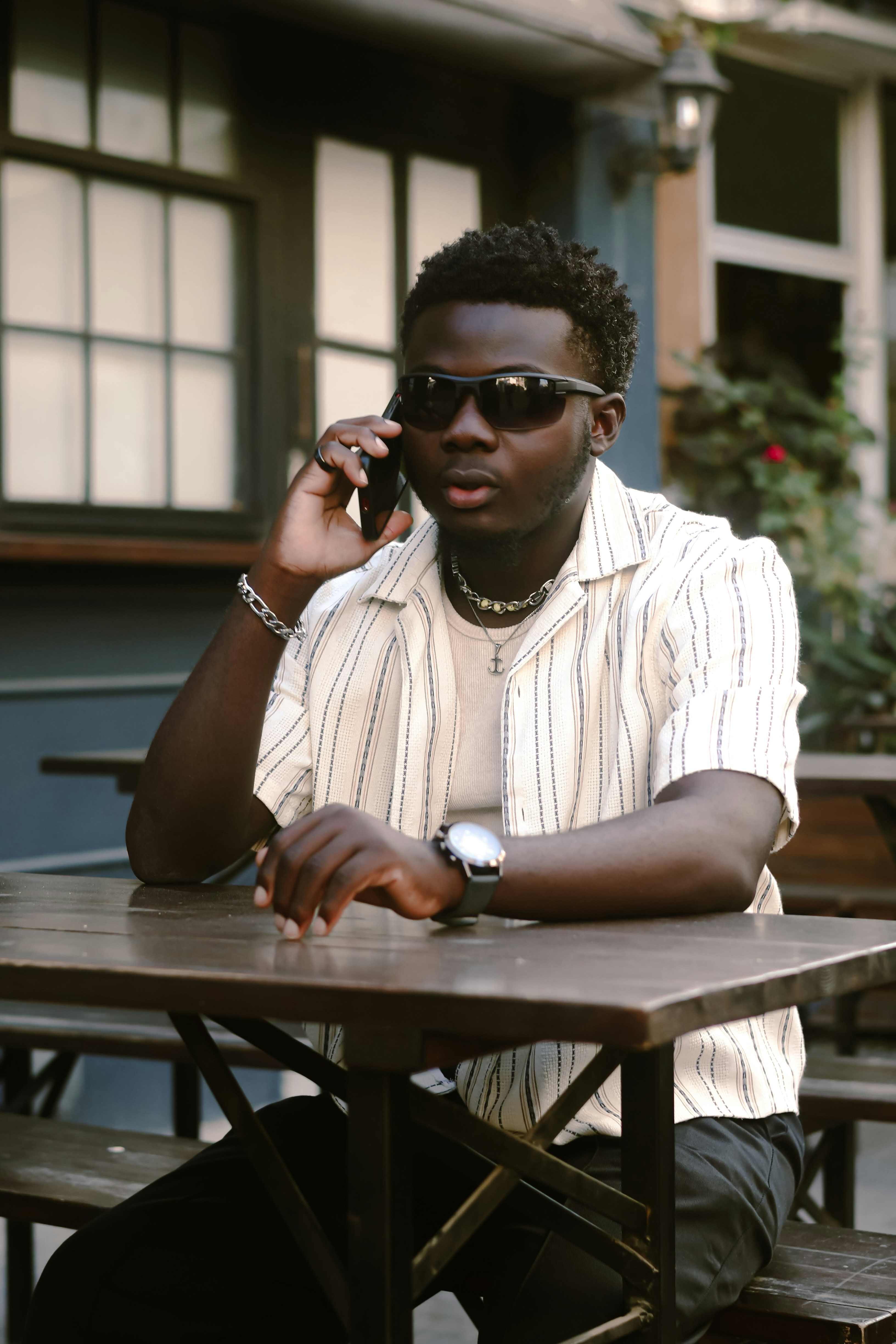 Man in sunglasses talks on phone at outdoor cafe.