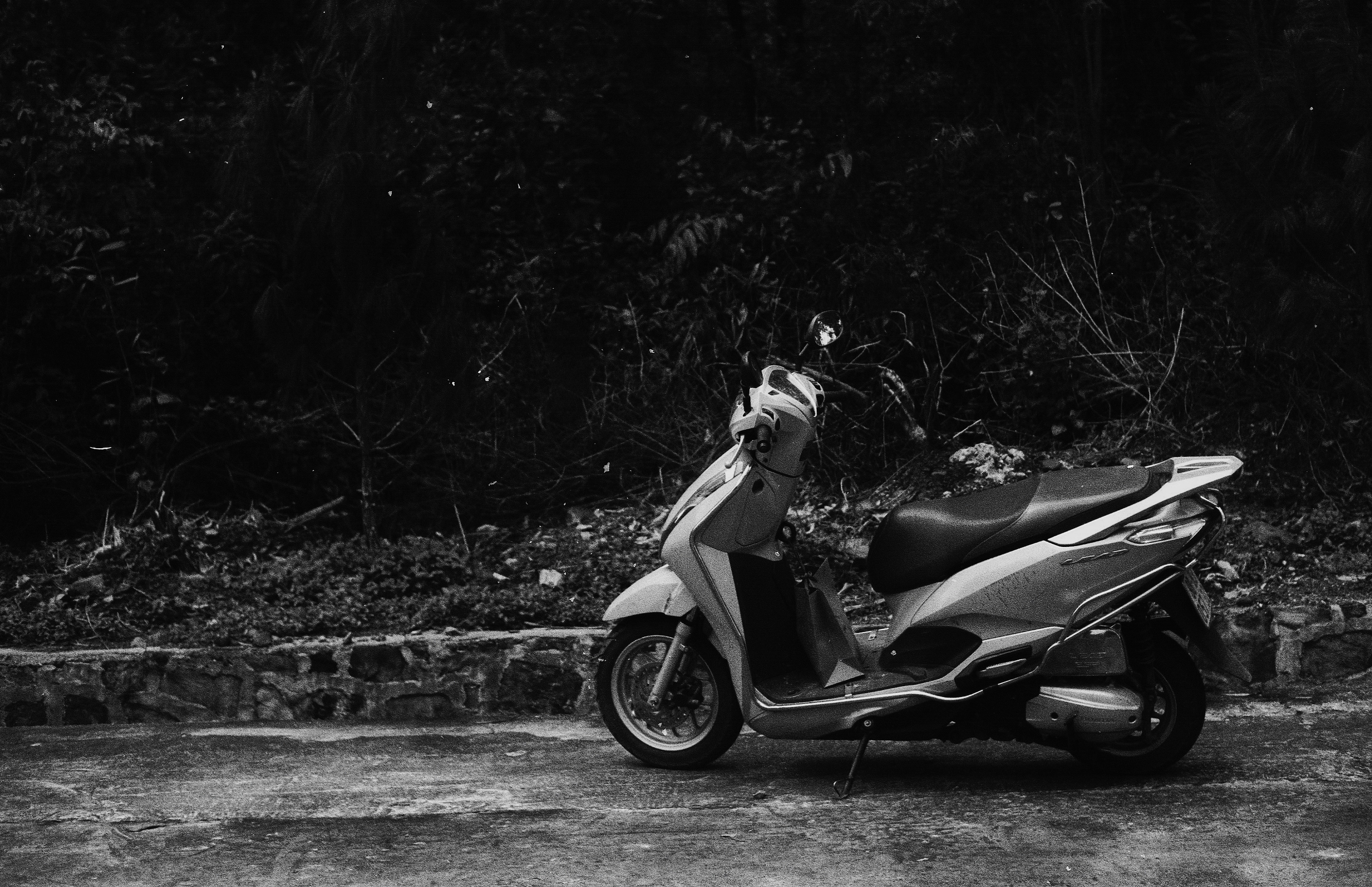 Skuter matik terparkir di tepi jalan, foto hitam putih