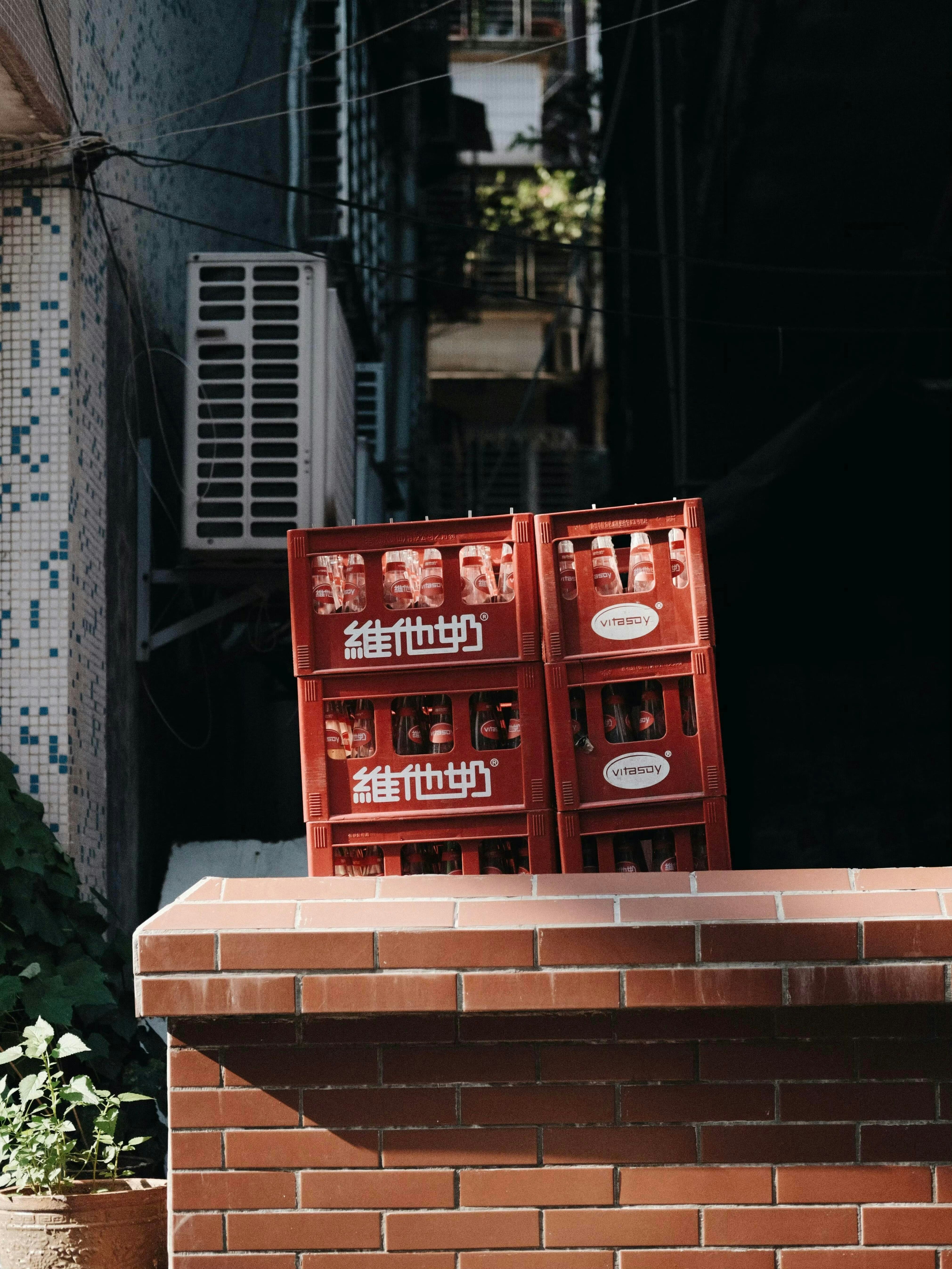 Des caisses rouges empilées contre un bâtiment dans une ruelle étroite.